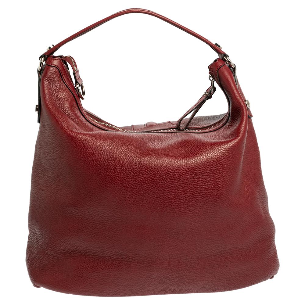 This Gucci creation is stylish, sophisticated & versatile. Crafted meticulously from grained leather, it carries a classy red shade. It is styled with a single handle that is anchored by silver-tone rings. The hobo flaunts a front flap pocket that