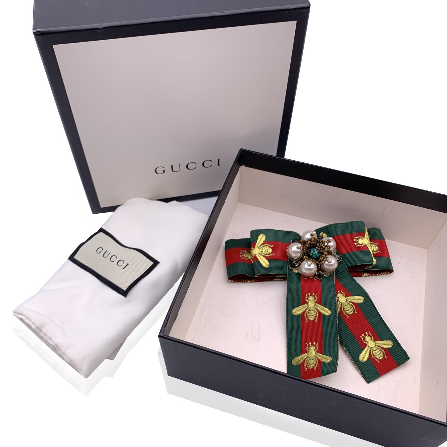 Beautiful Gucci green/red/green striped grosgrain bow brooch with embroidered bee. Pearls and rhinestones embellishment on the front.Safety pin closure on the back. Approx. width: 5.5 inches - 14 cm. Approx. height: 5.5 inches - 14 cm. Signed