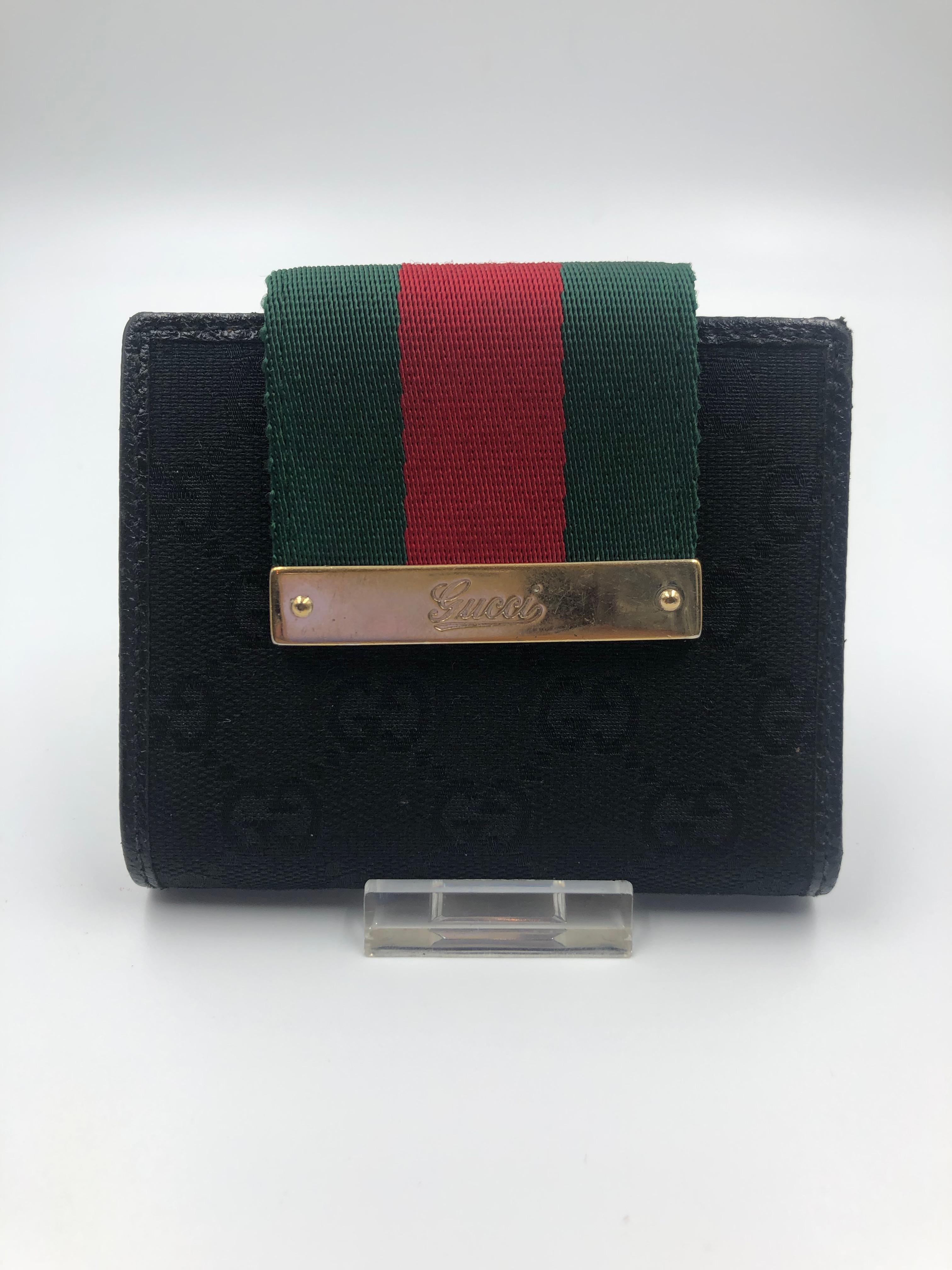 Gucci Red & Green Stripe Small Wallet. Black GG Logo fabric on front with black leather inside and back. Wallet closes with a metal snap. Contains change compartment on the back of the wallet. Wallet shows no signs of use.
4