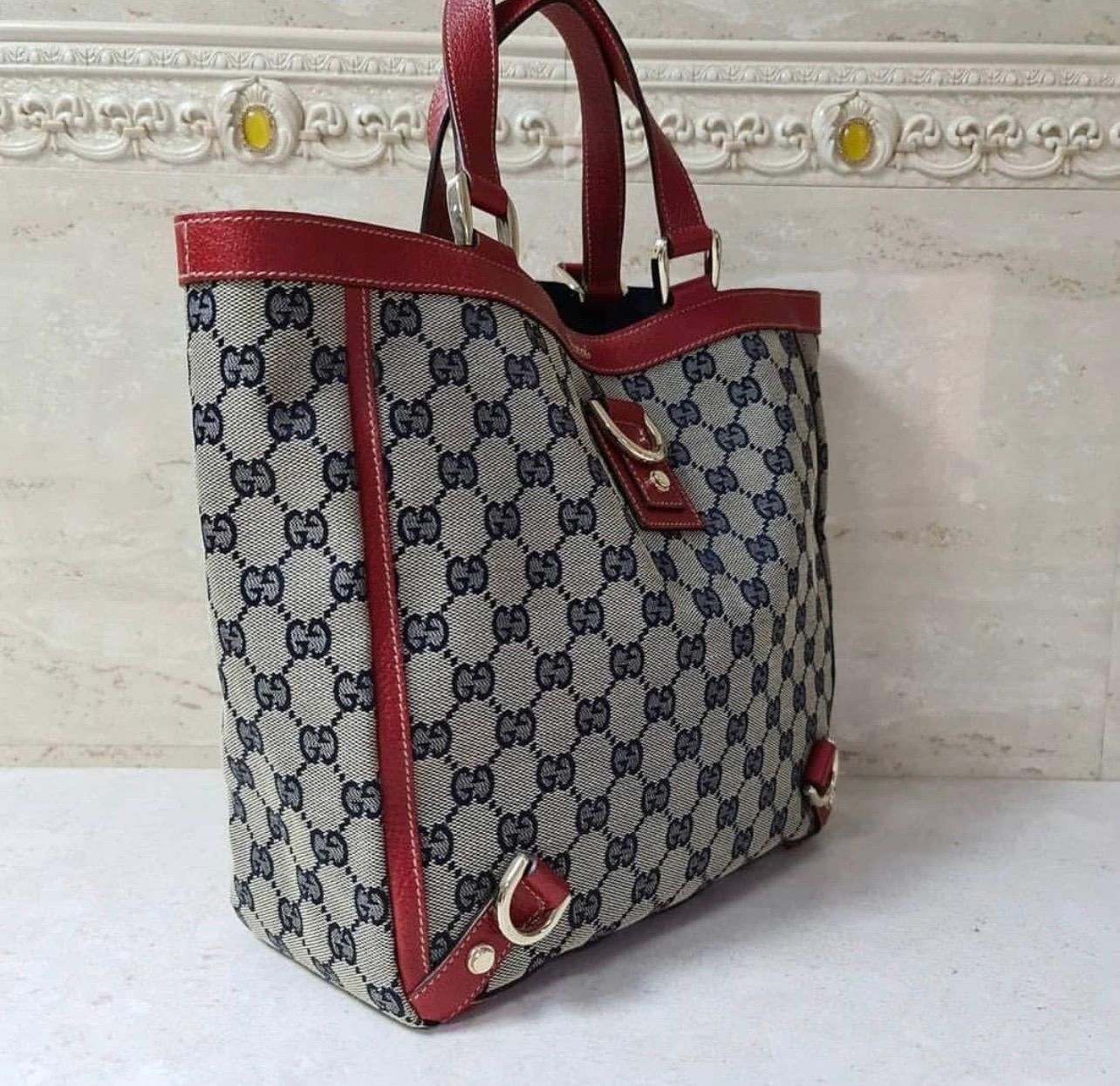 This is an authentic GUCCI Abbey D-Ring Tote.
 It's a sophisticated vintage Gucci tote for every day.
 It features a blue GG Monogram canvas with a red leather trim, short flat handles, gold-tone hardware, a d-rings on the front and back, and a