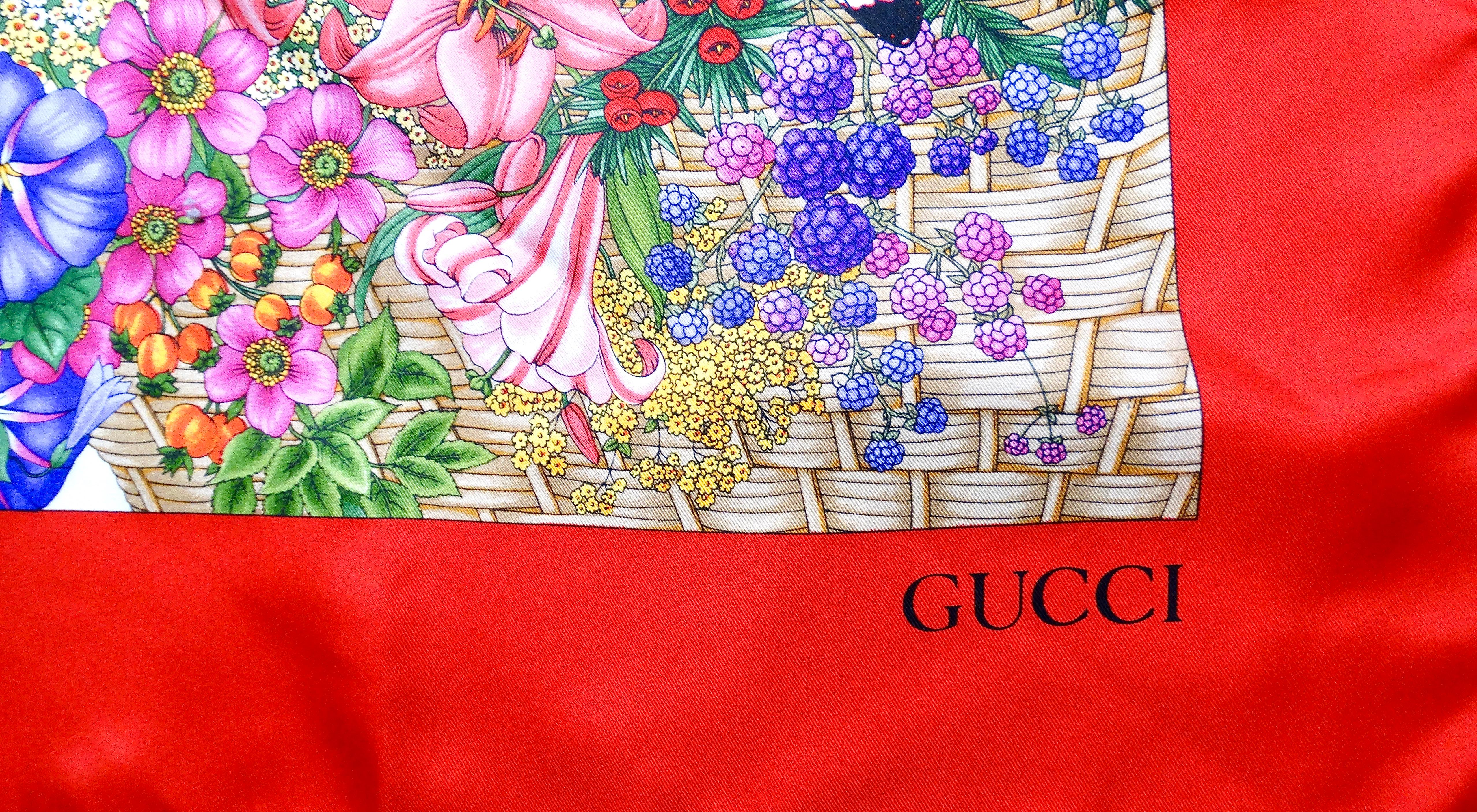 The Gucci Red & Multicolor Basket Of Flowers Motif Silk Scarf from the circa 1990s is a stunning example of vintage luxury craftsmanship. This luxurious scarf features a vibrant red base adorned with an intricate, multicolored floral basket motif