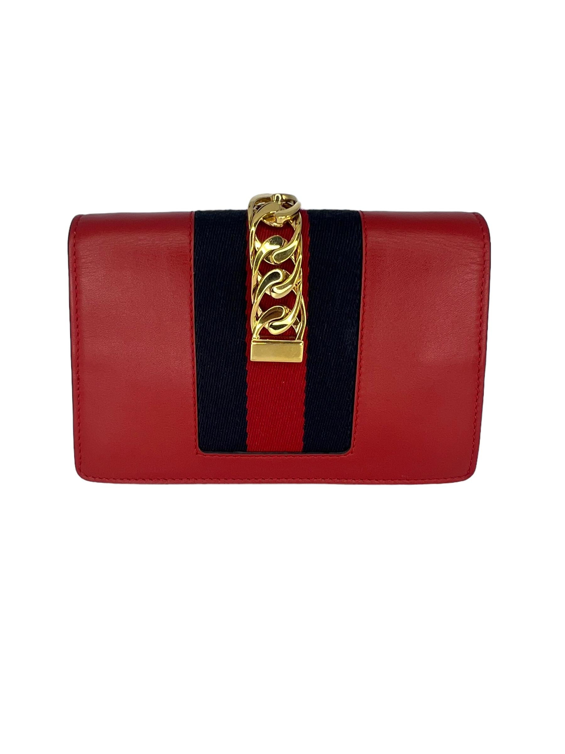 GUCCI Calfskin Mini Sylvie Chain Shoulder Bag in Hibiscus Red. This chic structured shoulder bag is crafted of smooth calfskin leather in red and features a gold chain strap, prominent front flap detailed with a central red and navy blue web stripe