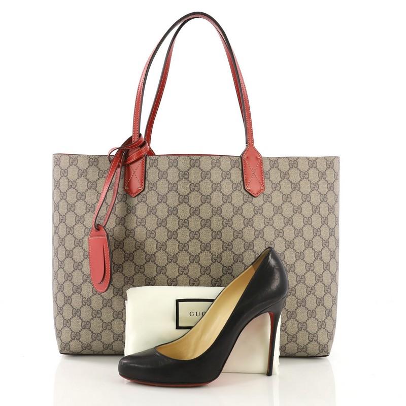 This Gucci Reversible Tote GG Print Leather Large, crafted from GG print leather, features dual flat leather handles. It opens to a reversible red leather interior. **Note: Shoe photographed is used as a sizing reference, and does not come with the