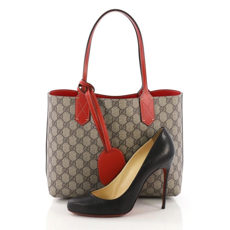 This Gucci Reversible Tote GG Print Leather Small, crafted from brown GG print coated canvas, features tall slim handles and subtle Gucci logo. Its wide top opens to a reversible red leather interior. **Note: Shoe photographed is used as a sizing