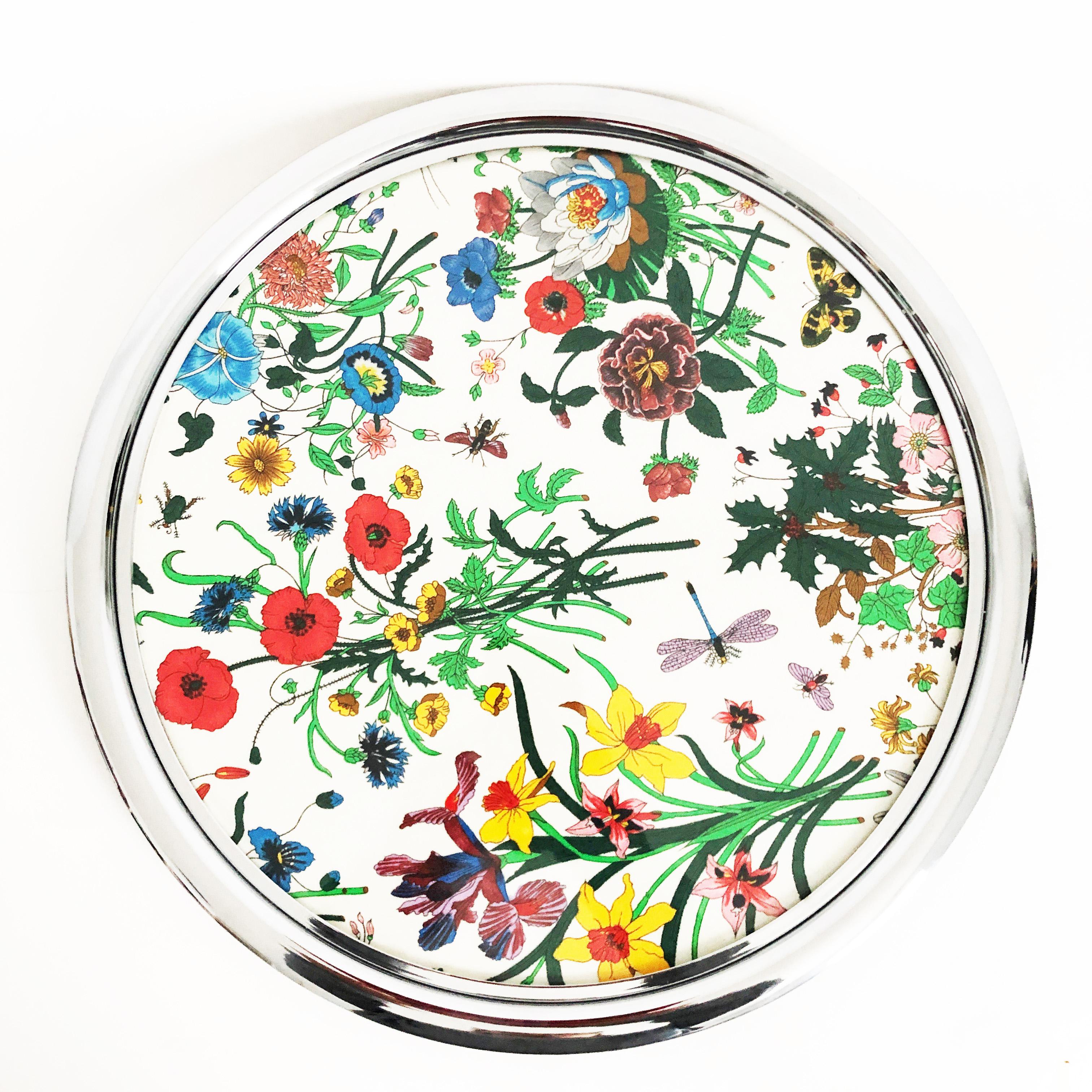 Entertain in style with this rare serving tray or platter from Gucci.  It features Accornero's iconic Flora motif on silk under plexiglas with a silver metal base.  It measures appx 14.5in diameter, making it perfect for serving cocktails or