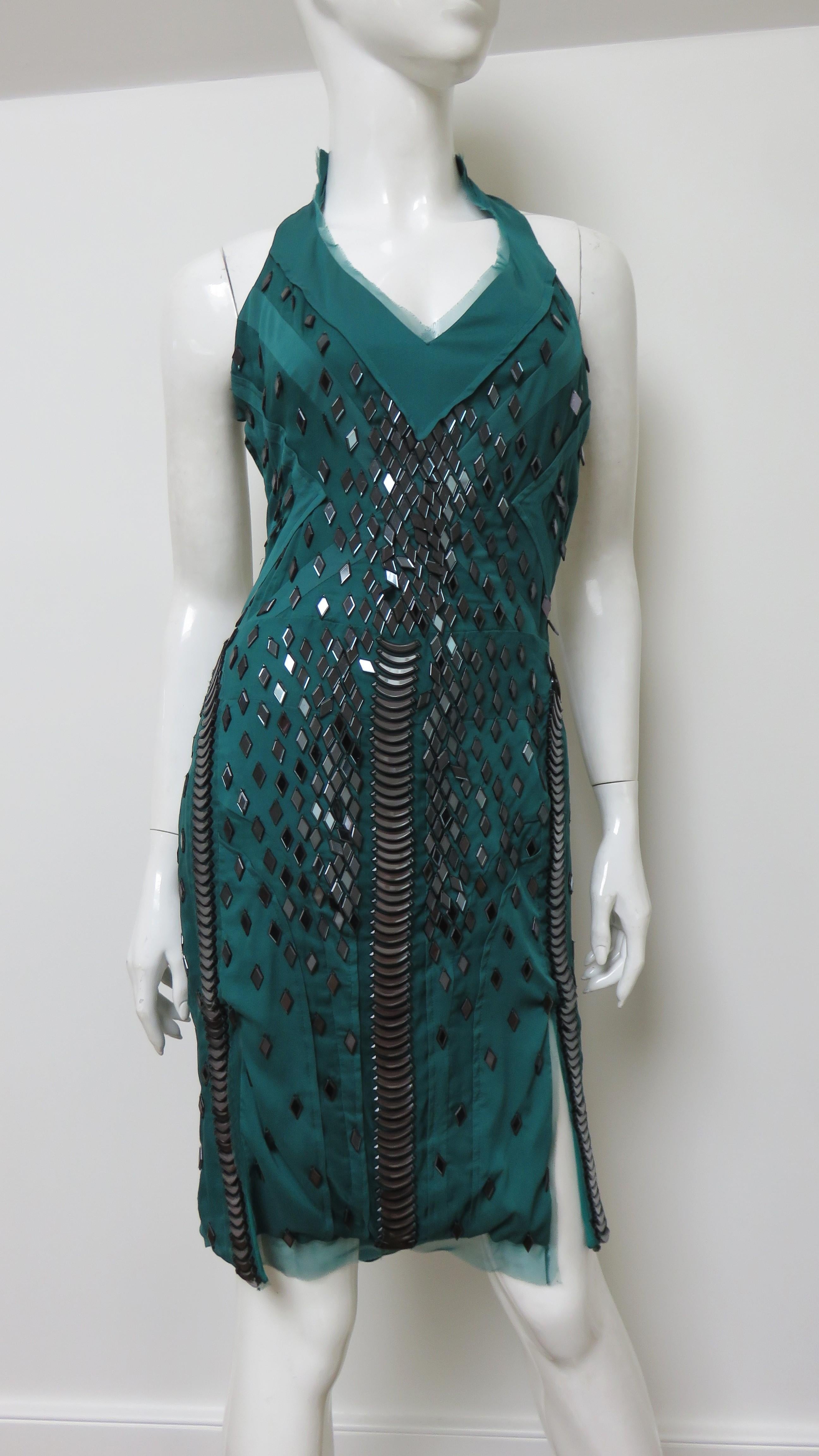 A gorgeous deep emerald green silk dress with elaborate appliques by Gucci.  It has a V neckline with cut in shoulders and a large back cut out with 2 matching straps across it. The dress is semi fitted with elaborate seaming and an abundance of