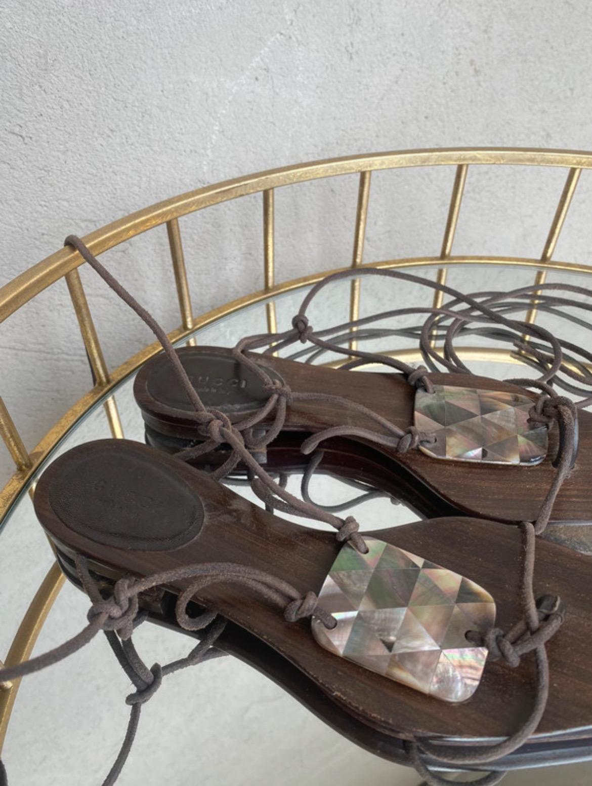 Sandali Gucci collezione 2002 di Tom Ford. In legno e pelle. Ha lacci in pelle e un inserto in madreperla.
Numero italiano 37C.
Soletta di 25 cm. Tacco 2 cm
In buone condizioni generali. Presenta normali segni di utilizzo.