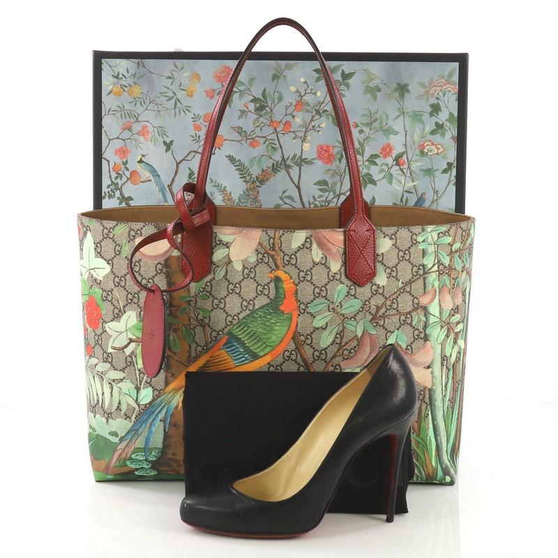 This Gucci Shopping Tote Tian Print GG Coated Canvas Medium, crafted from light brown GG coated canvas overlaid with Gucci Tian print, features dual flat handles, colorful array of birds and flowers, and silver-tone hardware. It's wide opening