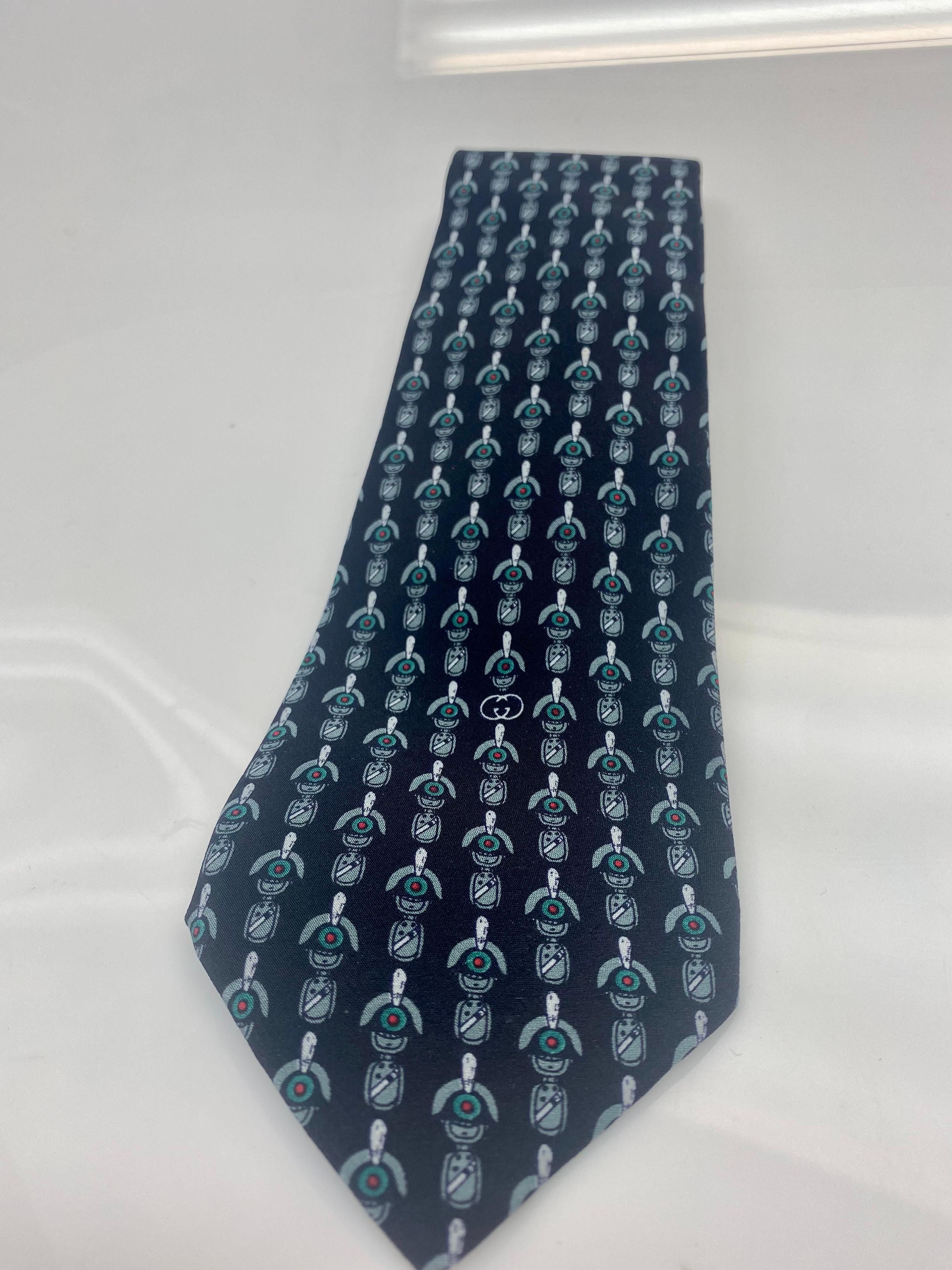 Cravate Gucci en soie imprimée noir, vert et blanc. 
Une pièce sophistiquée et classique qui s'intègre parfaitement à toute garde-robe. L'article est en bon état, usure conforme à l'âge. 

Largeur : 3.3