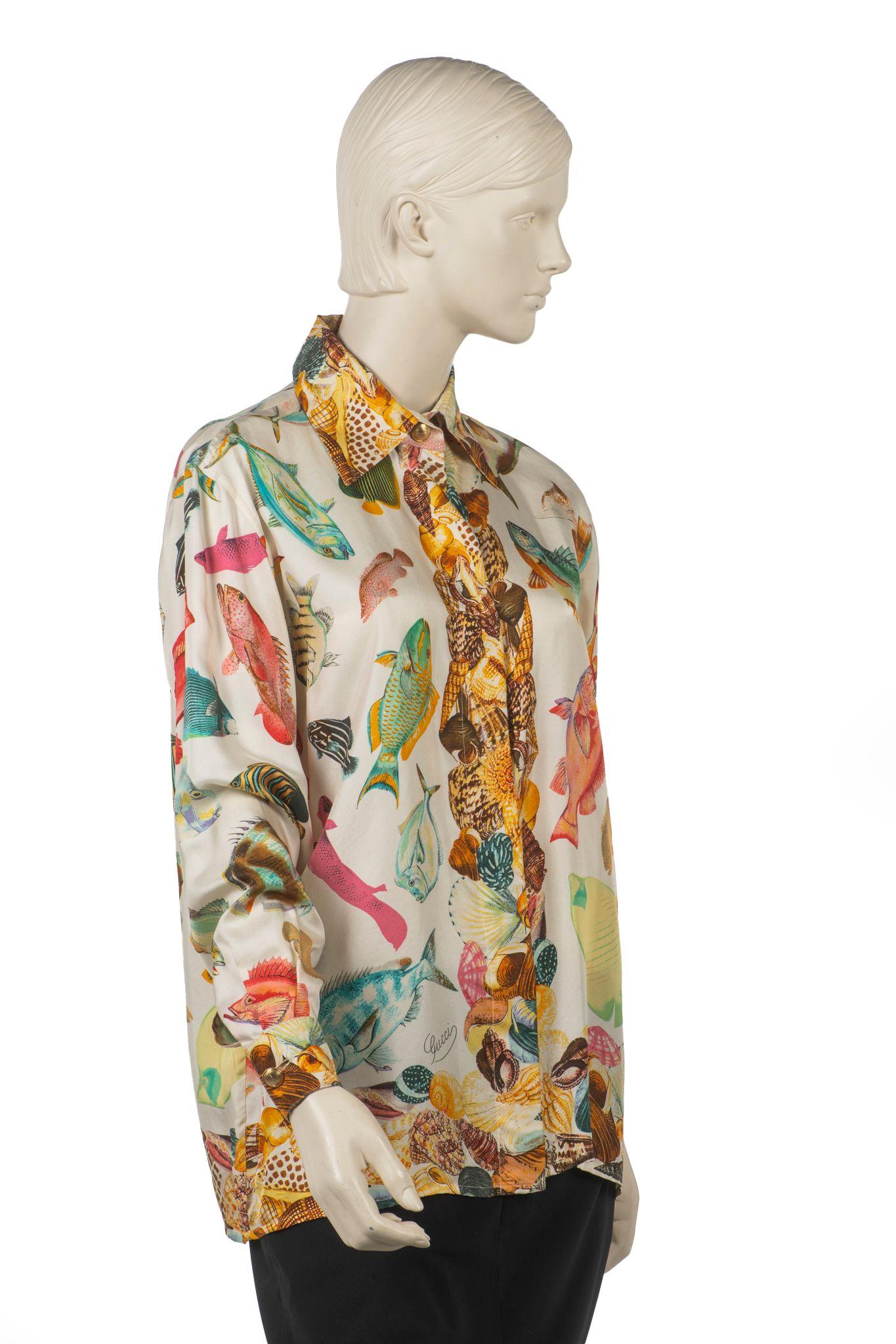 Cette chemise à boutons Gucci présente un motif de poisson coloré et des boutons en nacre embossés Gucci cachés dans une patte de boutonnage sur le devant. Un bouton Gucci en métal doré est apposé au niveau du col et des poignets des manches