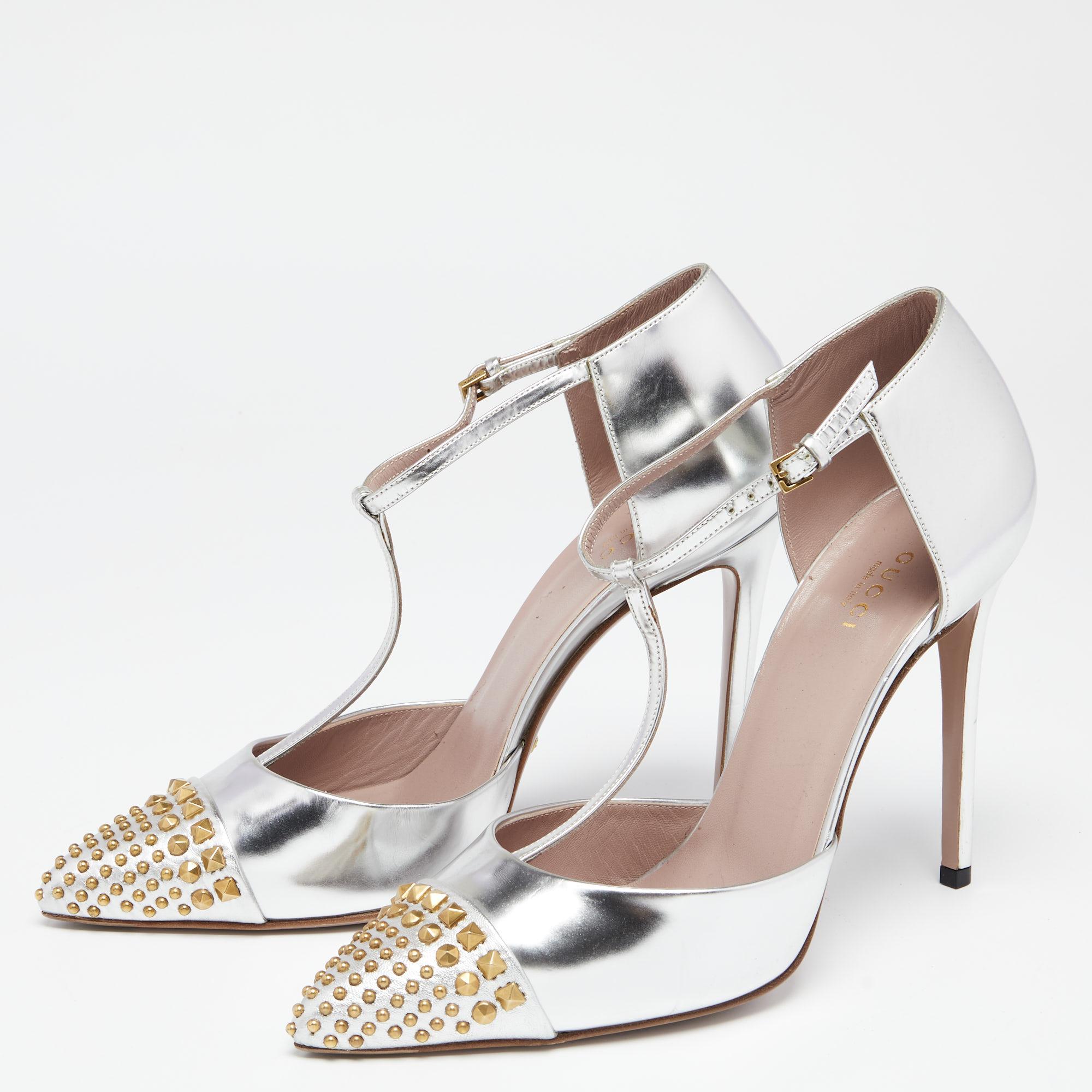 These stunning Coline pumps are a true testament to Gucci's unique style and skilled design. They are made from silver leather and comprise a T-strap, gold-toned studded pointed toes, and sleek heels. Match them with your outfit to flaunt a luxe