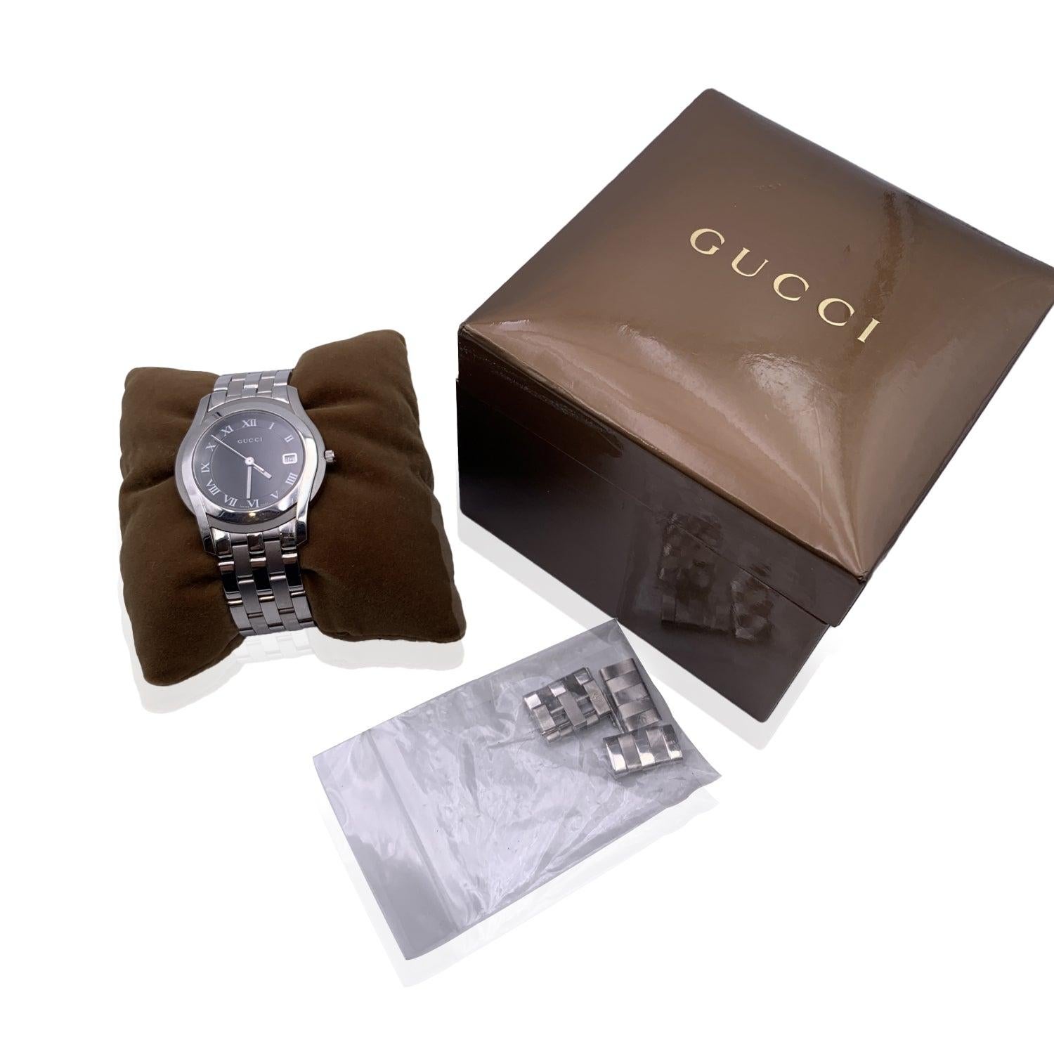 Gucci silver tone stainless steel wrist watch, mod. 5500 M. Black Dial. Date at 3 o'clock. Sapphire crystal. Swiss Made Quartz movement. Gucci written on face. Roman numbers. Gucci crest on the reverse of the case. Water Resistant to 3atm. Stainless