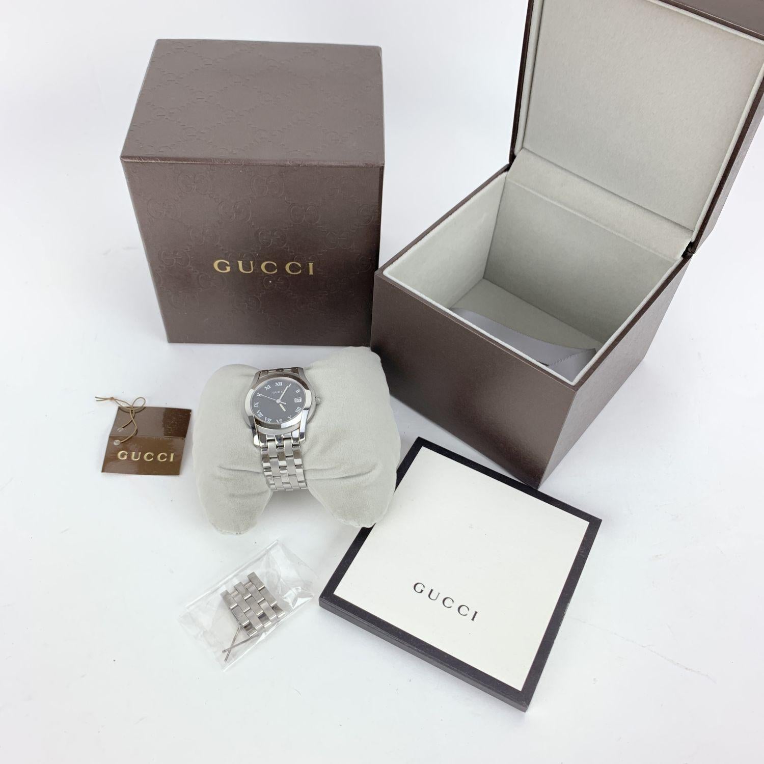 Gucci silver tone stainless steel wrist watch, mod. 5500 M. Black Dial. Date at 3 o'clock. Sapphire crystal. Swiss Made Quartz movement. Gucci written on face. Roman numbers. Gucci crest on the reverse of the case. Water Resistant to 3atm. Stainless
