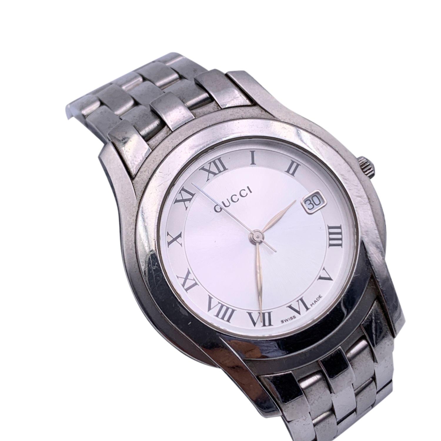 Gucci silver tone stainless steel wrist watch, mod. 5500 M. Silver Dial. Date at 3 o'clock. Sapphire crystal. Swiss Made Quartz movement. Gucci written on face. Roman numbers. Gucci crest on the reverse of the case. GUCCI logo engraved on the clasp.