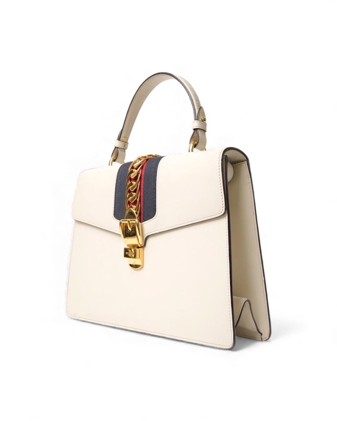 Borsa firmata Gucci, modello Silvye nella misura large, realizzata in pelle box bianca con hardware dorato. Dotata di una patta con chiusura ad incastro, internamente rivestita in tessuto scamosciato beige con comoda tasca, la borsa è abbastanza