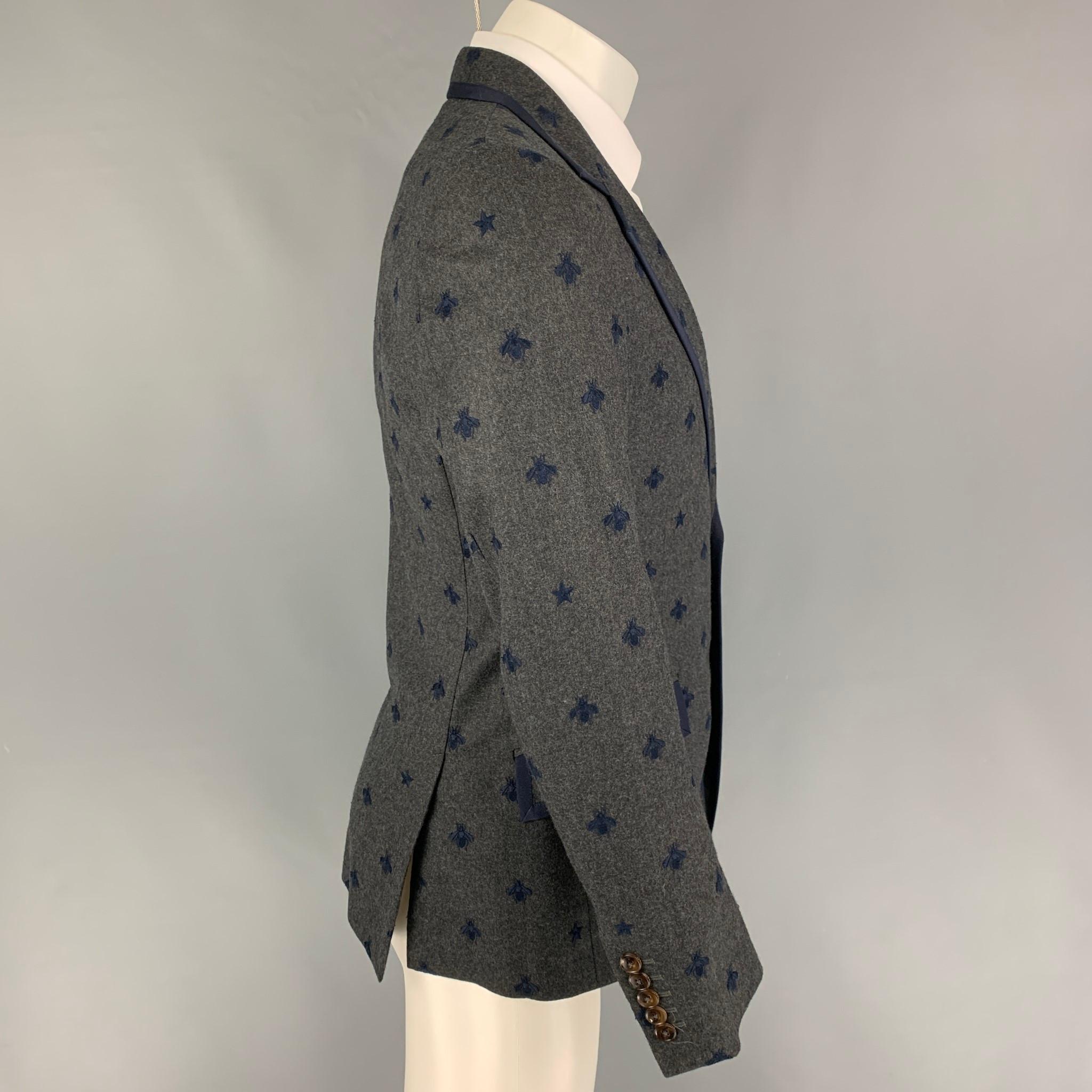 GUCCI sport coat comes in a charcoal wool with a full liner featuring navy 'Royal Bee' embroidery details, notch lapel, flap pocket, double back vent, and a two button closure. Made in Italy. 

Excellent Pre-Owned Condition.
Marked: 46