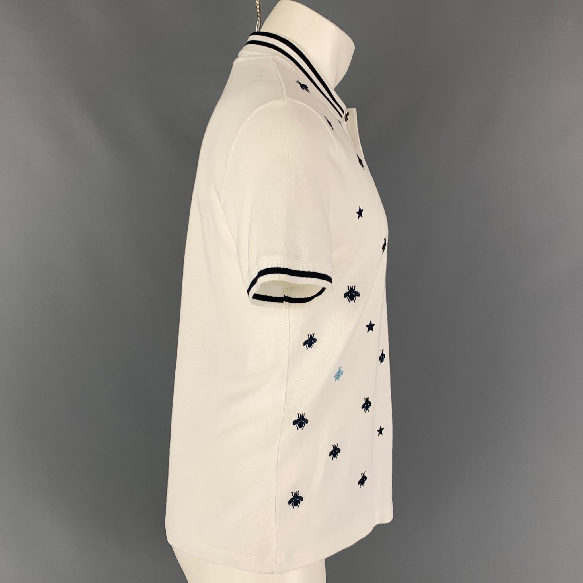 GUCCI polo comes in a white & navy material with a 'Bees & Stars' embroidered design featuring a stripe trim and a buttoned closure. Made in Italy. 

Good Pre-Owned Condition. Minor marks at sleeve.
Marked: Size tag removed.
Original Retail Price: