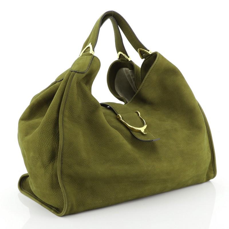 This Gucci Soft Stirrup Tote Nubuck Large, crafted in green nubuck, features side to side looped dual-flat handles with unique spur detailing and gold-tone hardware. Its slide flap closure opens to a neutral fabric interior with side zip and slip