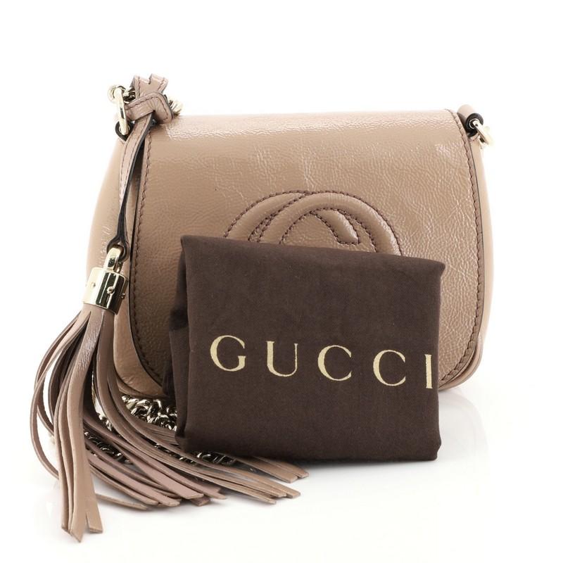 This Gucci Soho Chain Crossbody Bag Patent Small, crafted from pink patent leather, features chain link strap, tassel accent, stitched interlocking GG logo, and gold-tone hardware. Its hidden magnetic snap closure opens to a neutral fabric interior
