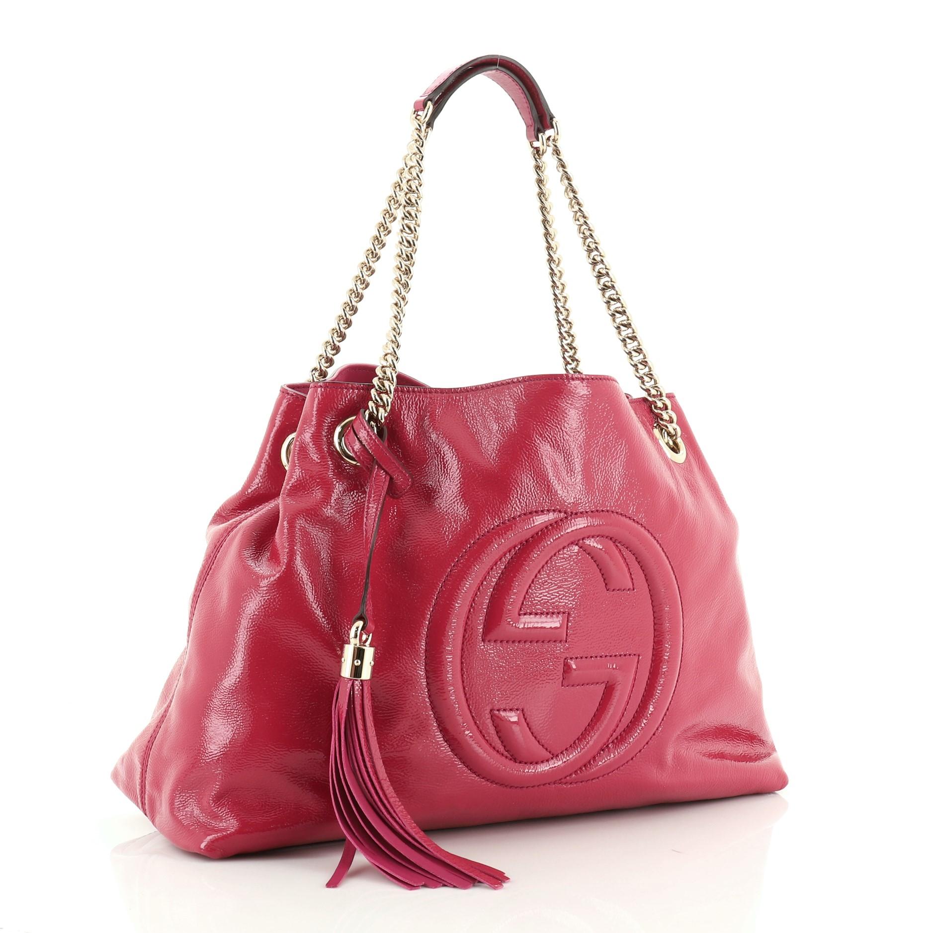 This Gucci Soho Chain Strap Shoulder Bag Patent Medium, crafted in pink patent leather, features chain link straps with leather pads and gold-tone hardware. Its hook clasp closure opens to a neutral fabric interior with side zip and slip pockets.