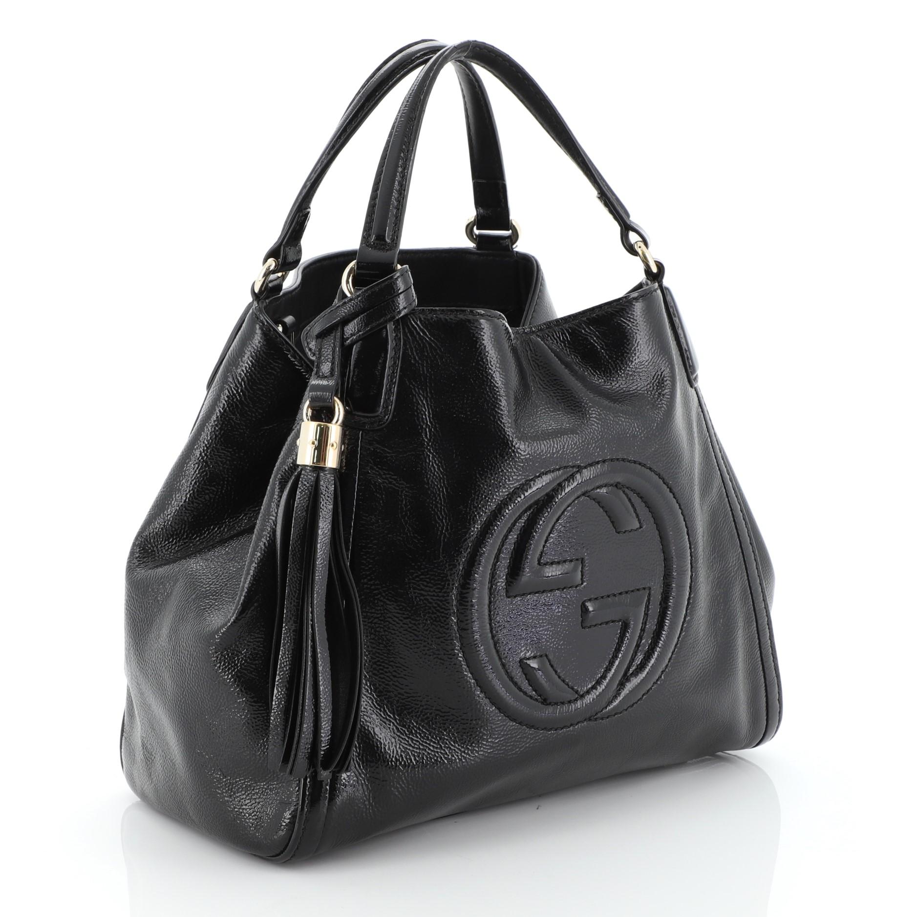 This Gucci Soho Convertible Shoulder Bag Patent Small, crafted from black patent leather, interlocking GG logo stitched at the front, dual looped top handles, protective base studs, and gold-tone hardware. Its hook clasp closure opens to a black