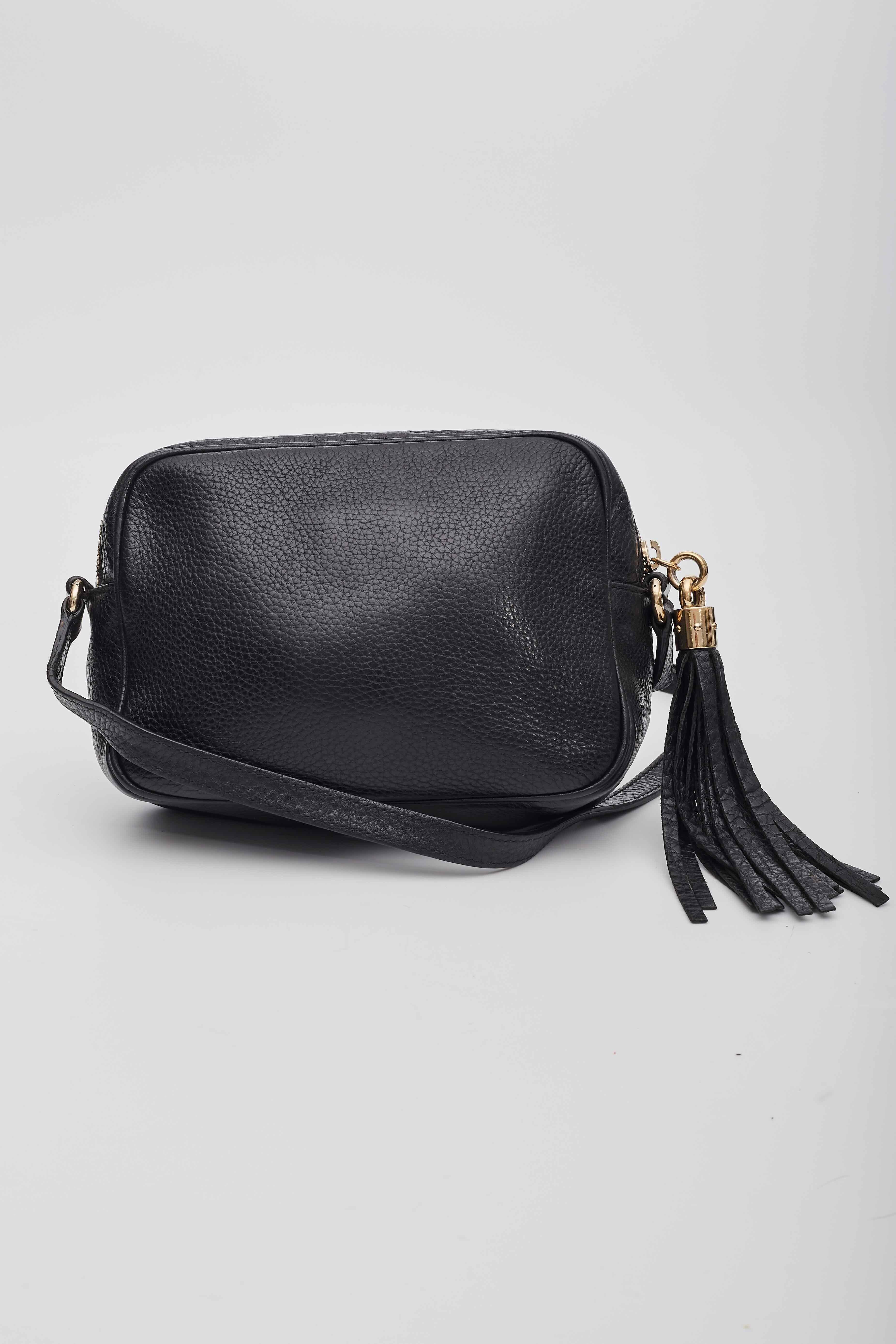 This crossbody bag is made of pebbled calfskin leather in black, with a prominent Gucci GG logo stitched on the front. The bag features an adjustable leather shoulder strap with polished gold hardware. The matching gold-knobbed leather tassel zipper