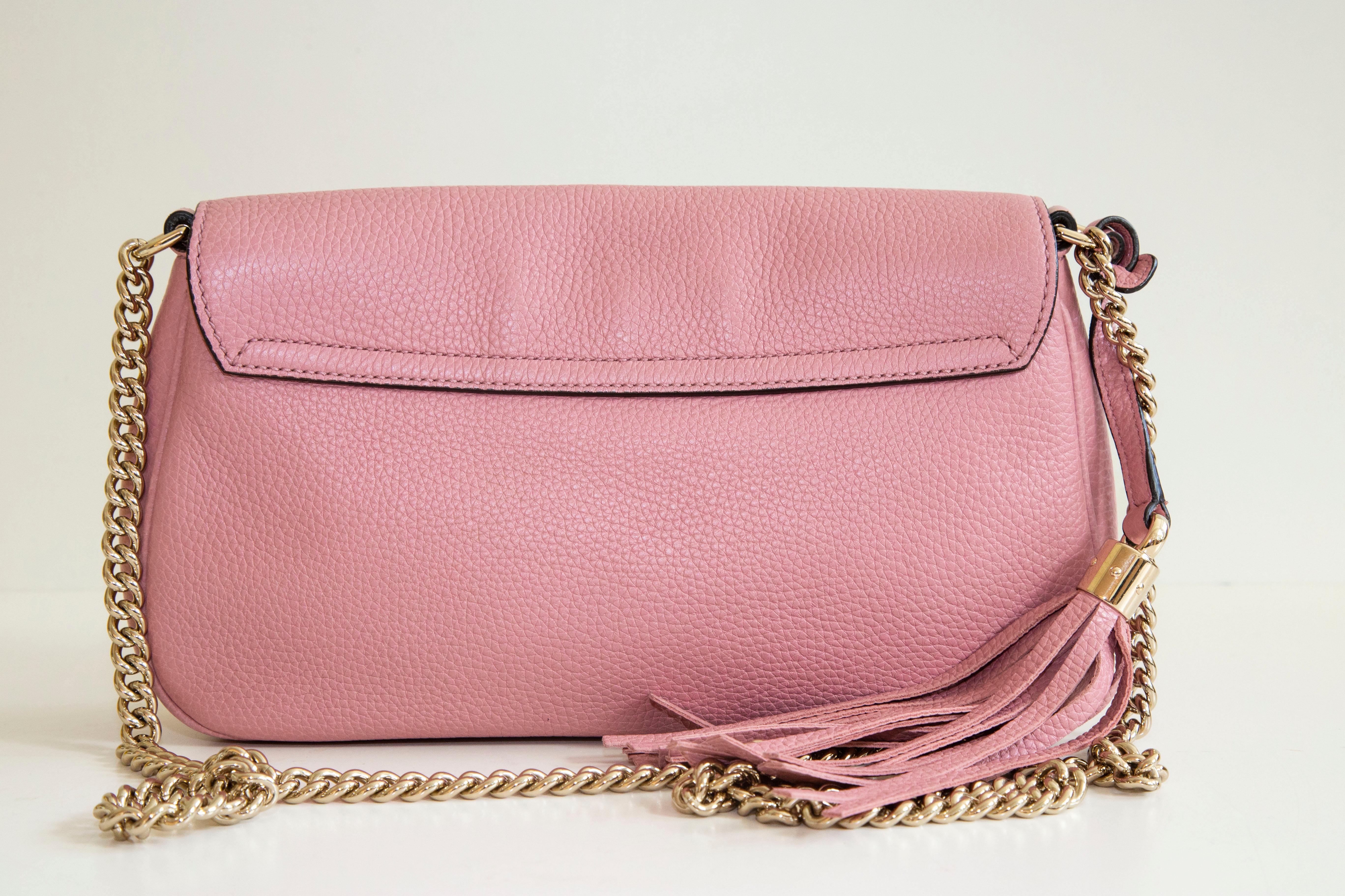 A Gucci Soho pink leather crossbody bag with chain strap. The bag features a front flap with a magnetic closure. The main compartment is lined with light beige fabric and it contains 2 side pockets of which one has a zipper. The interior is neat and
