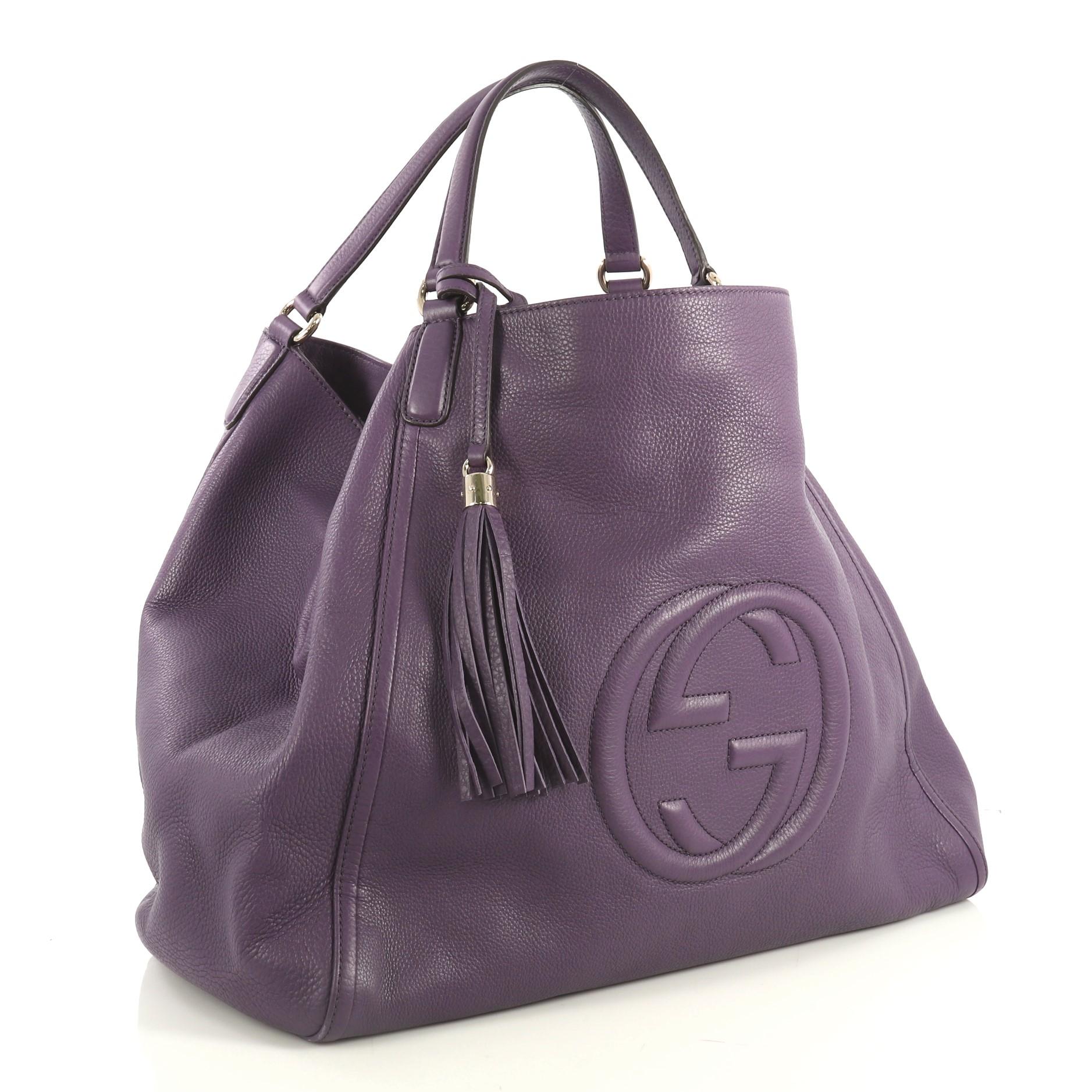 This Gucci Soho Shoulder Bag Leather Large, crafted from purple leather, features dual leather handles, fringe tassel, interlocking Gucci logo stitched in front, and gold-tone hardware. Its open top with hook closure opens to a neutral fabric