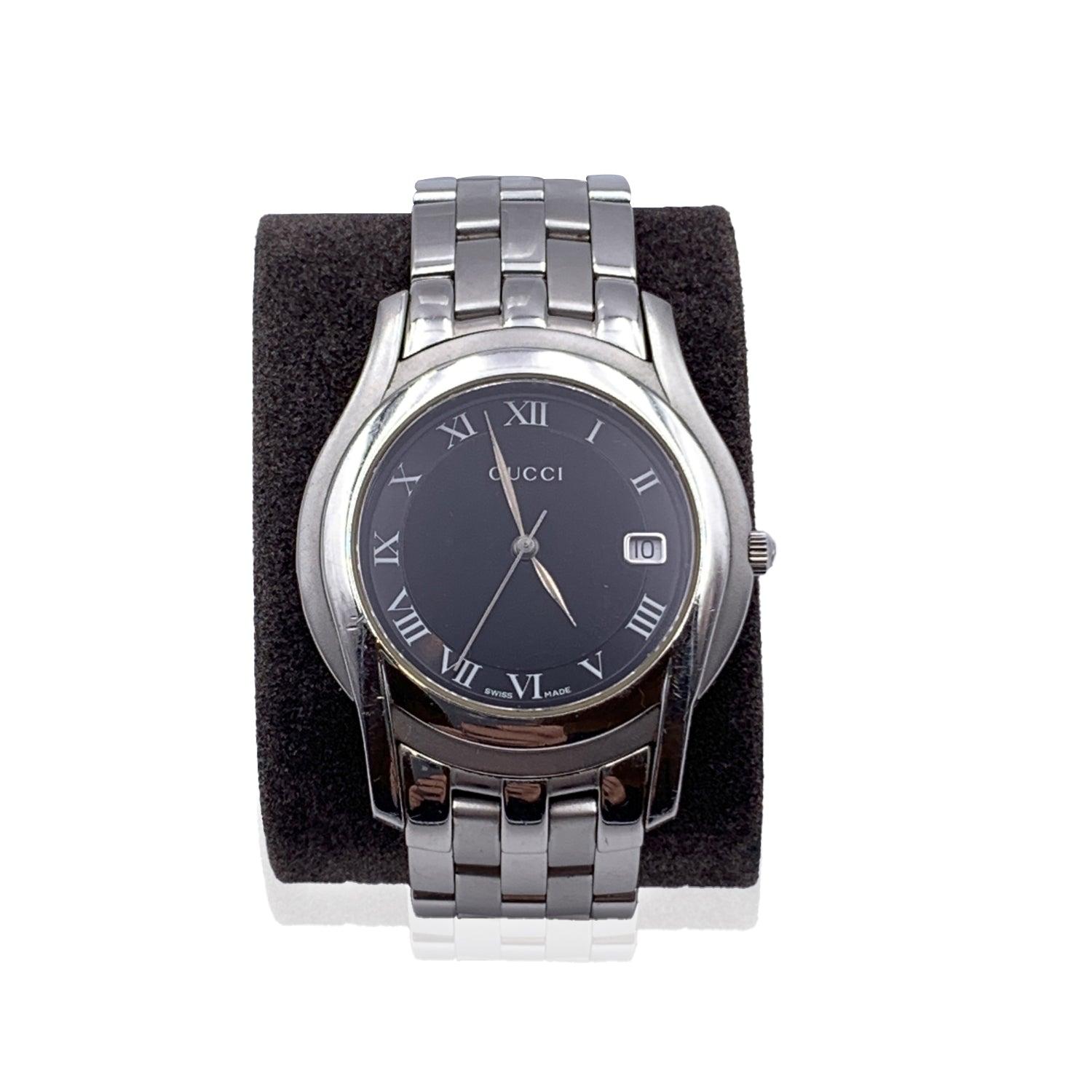 Gucci silver tone stainless steel wrist watch, mod. 5500 M. Black Dial. Date at 3 o' clock. Sapphire crystal. Swiss Made Quartz movement. Gucci written on face. Roman numbers. Gucci crest on the reverse of the case. Water Resistant to 3atm.