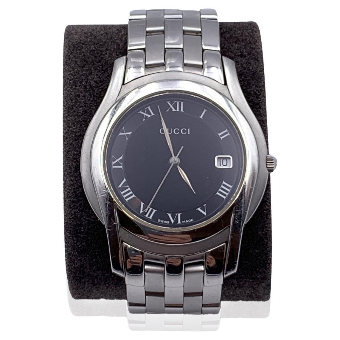 Gucci silver tone stainless steel wrist watch, mod. 5500 M. Black Dial. Date at 3 o' clock. Sapphire crystal. Swiss Made Quartz movement. Gucci written on face. Roman numbers. Gucci crest on the reverse of the case. Water Resistant to 3atm.