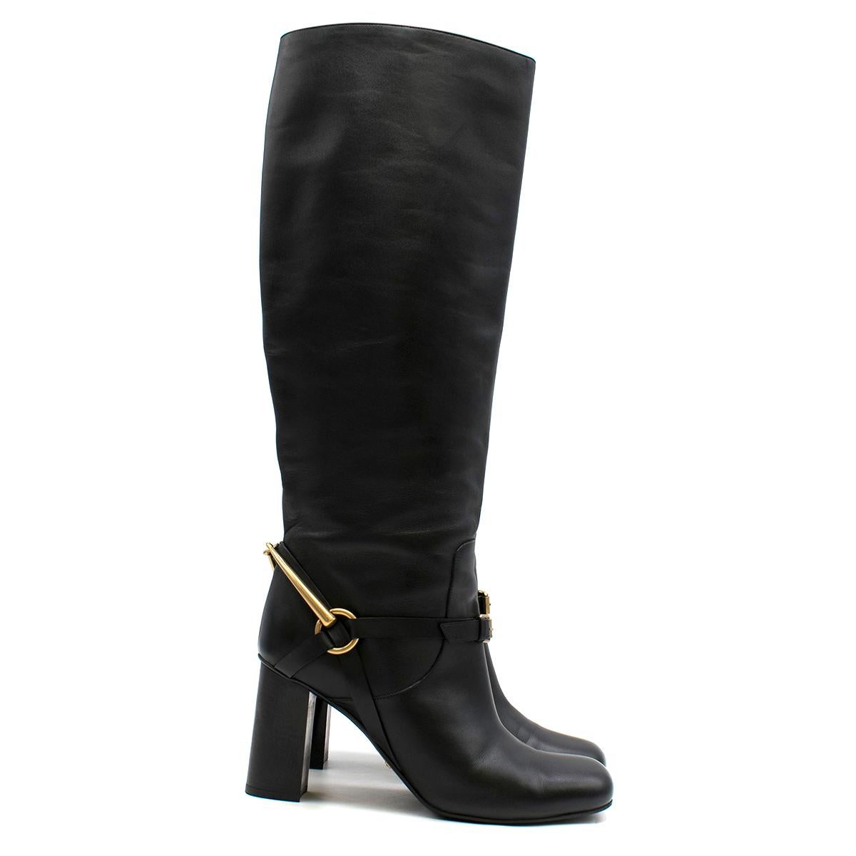 Gucci stirrup-heel leather boots 

- Black, smooth leather 
- Rounded square toe, high stacked leather block heel
- Antiqued gold-tone metal stirrup-effect heel feature
- Buckle-fastening arch strap 
- Black leather lining and insole 
- Black