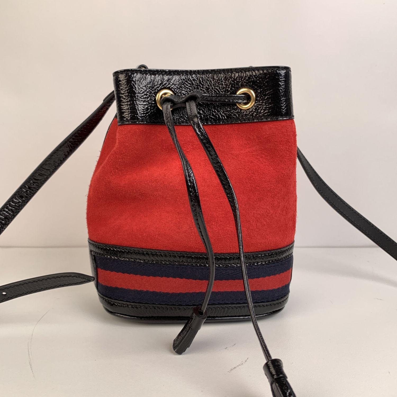 Gucci Ophidia small bucket bag in red suede with black patent leather trim. Blue/Red/Blue signature web detailing on the bottom part of the bag. Drawstring closure on top. Adjustable shoulder strap. Beige suede lining. 'GUCCI - made in Italy' tag