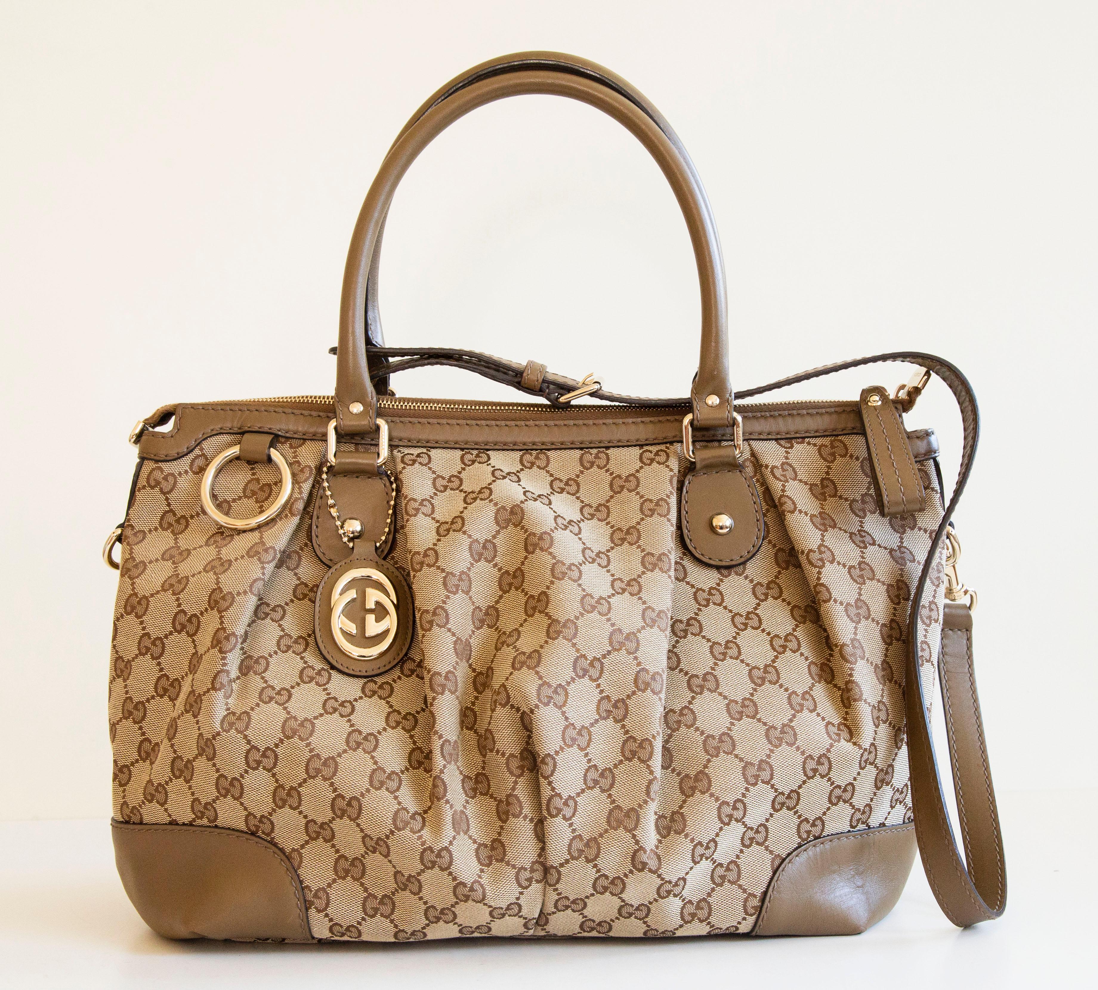 An authentic Gucci Sukey two-way bag. The bag can be both worn as a top handle bag or as a crossbody bag, the strap is removable. The bag features a GG canvas, brownish/ochre leather trim, and gold-tone hardware. The interior is lined with beige