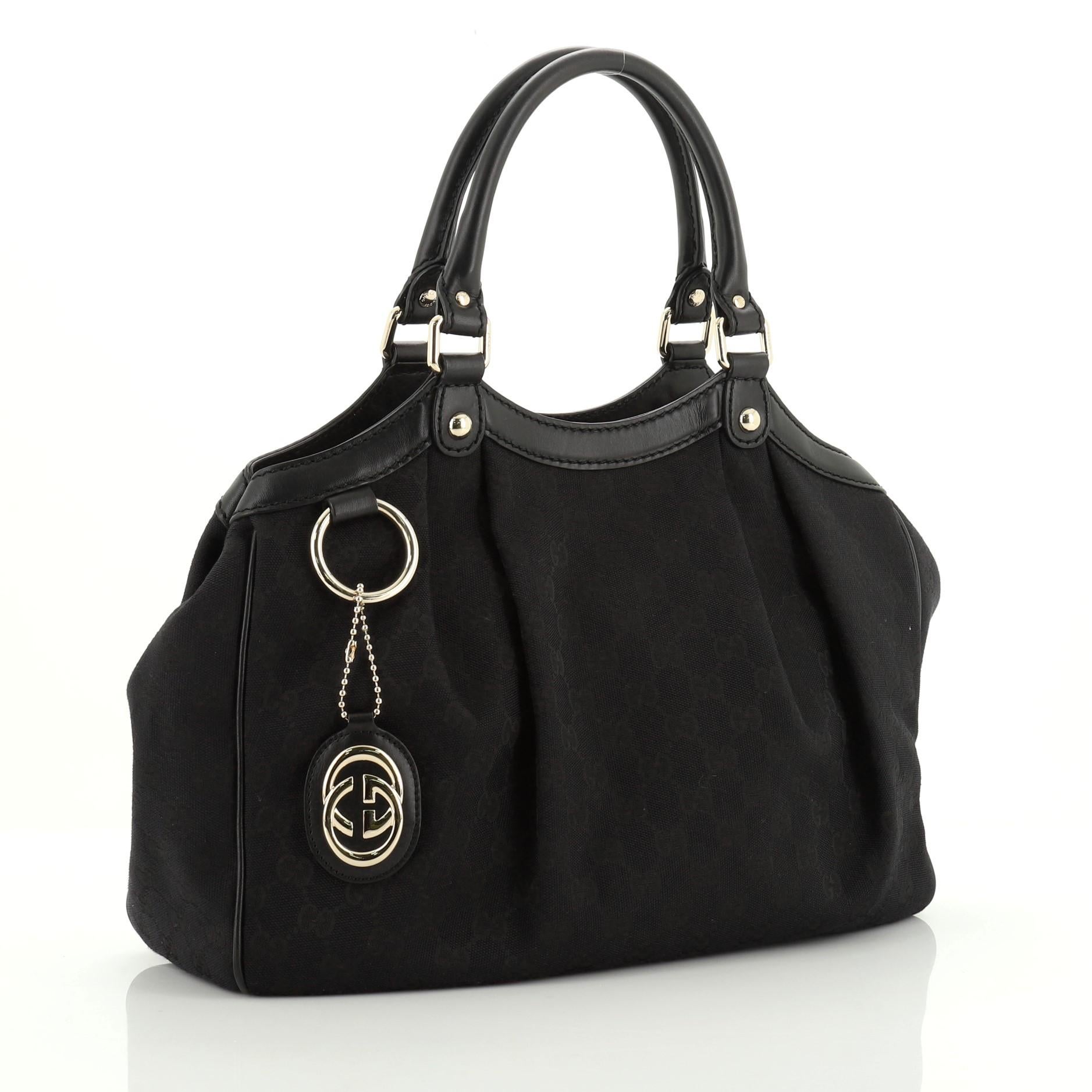 This Gucci Sukey Tote GG Canvas Medium, crafted from black GG canvas, features dual rolled leather handles, leather trim, and gold-tone hardware. Its magnetic snap closure opens to a neutral fabric and canvas interior with side zip pocket.