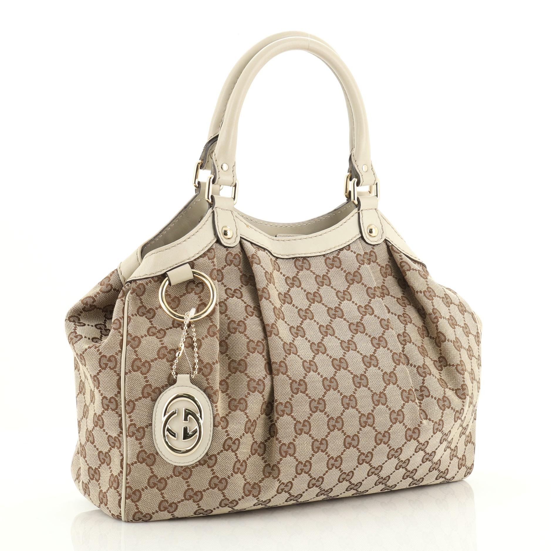 This Gucci Sukey Tote GG Canvas Medium, crafted from brown GG canvas, features dual rolled leather handles, leather trim, and gold-tone hardware. Its magnetic snap closure opens to a brown fabric interior with side zip pocket. 

Estimated Retail