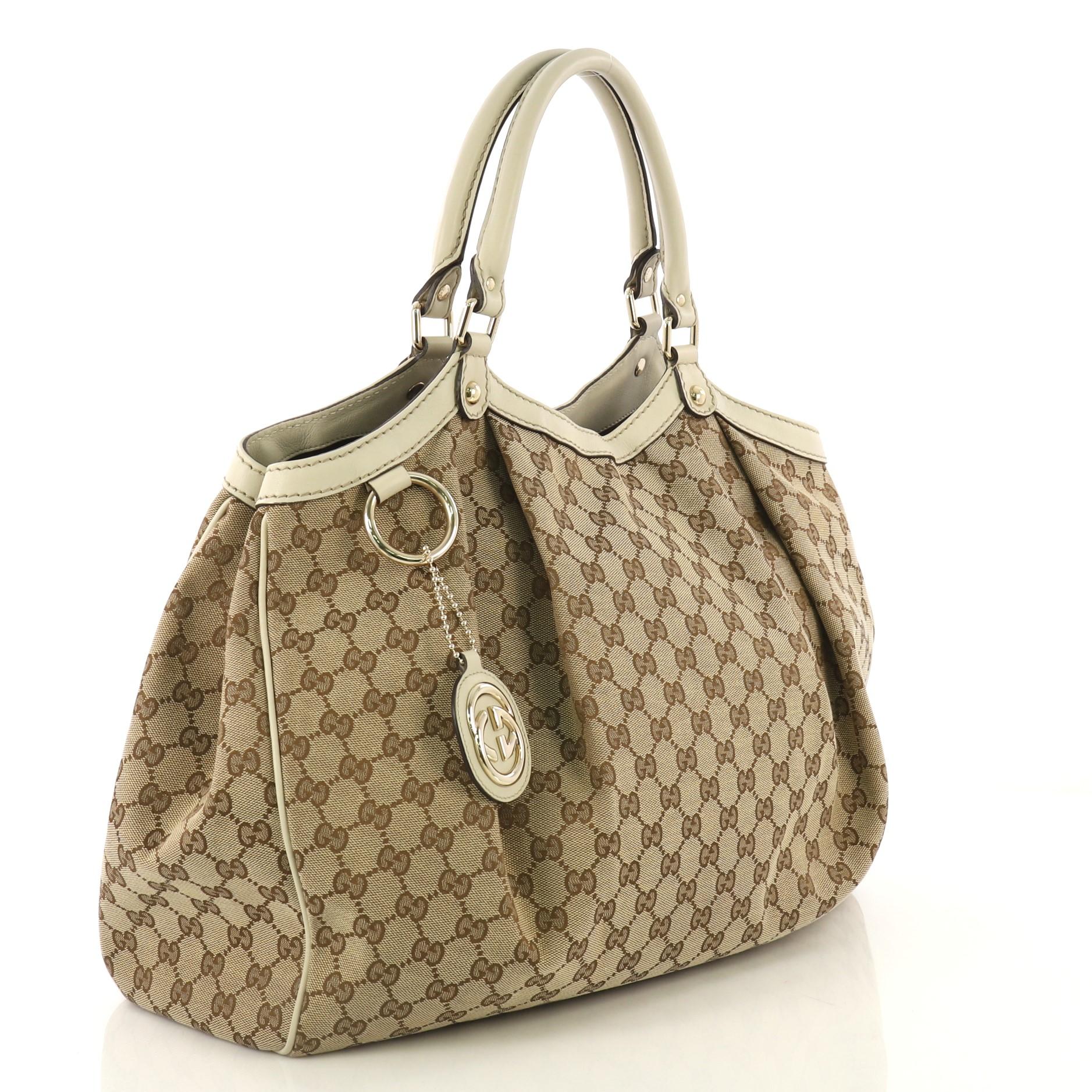 This Gucci Sukey Tote GG Canvas Large, crafted from brown GG canvas and light gray leather, features dual rolled leather handles, leather trim, and gold-tone hardware. Its magnetic snap closure opens to a dark brown fabric interior with zip pocket.
