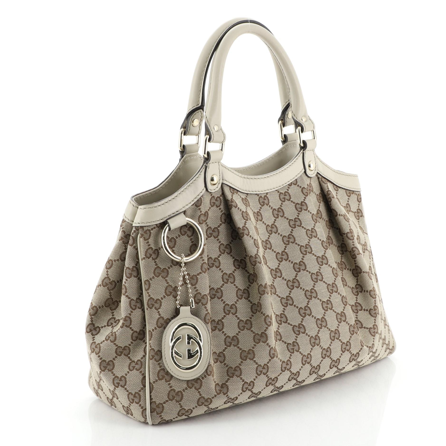 This Gucci Sukey Tote GG Canvas Medium, crafted from brown GG canvas, features dual rolled leather handles, side snap buttons, and gold-tone hardware. Its magnetic snap closure opens to a neutral fabric and canvas interior with zip pocket.