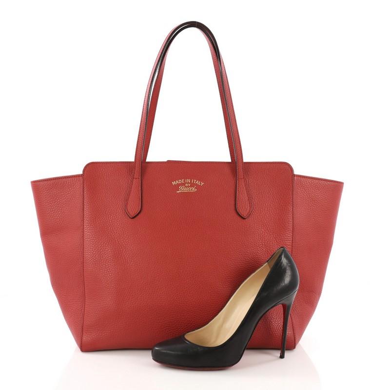 This Gucci Swing Tote Leather Medium, crafted in red leather, features dual slim handles, Gucci stamped logo at the front, expanded wing silhouette, and gold-tone hardware. Its hidden magnetic snap closure opens to a beige canvas interior with side