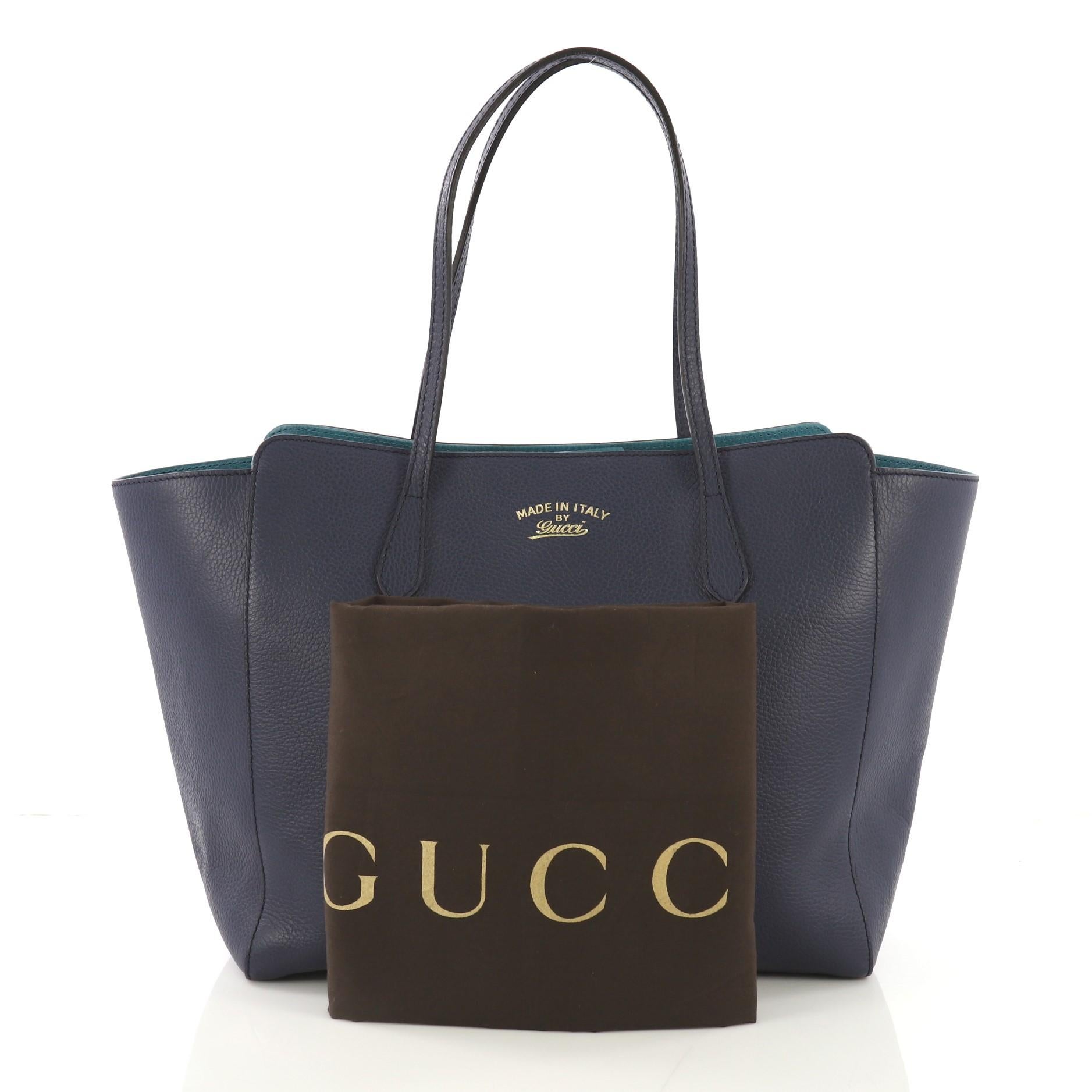 This Gucci Swing Tote Leather Medium, crafted in blue leather, features dual slim handles, Gucci stamped logo at the front, expanded wing silhouette, and gold-tone hardware. Its hidden magnetic snap closure opens to a beige fabric interior with side