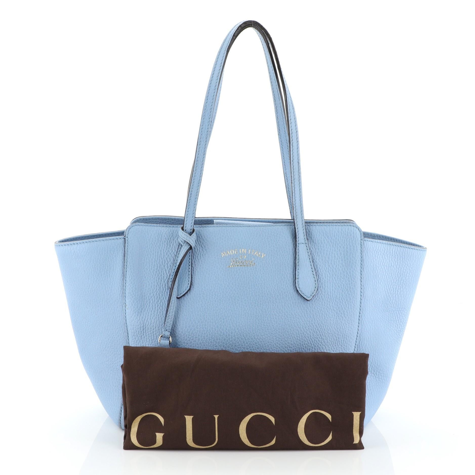 This Gucci Swing Tote Leather Small, crafted in blue leather, features dual slim handles, Gucci stamped logo at the front and gold-tone hardware. Its hidden magnetic snap closure opens to a neutral fabric interior with zip and slip pockets.