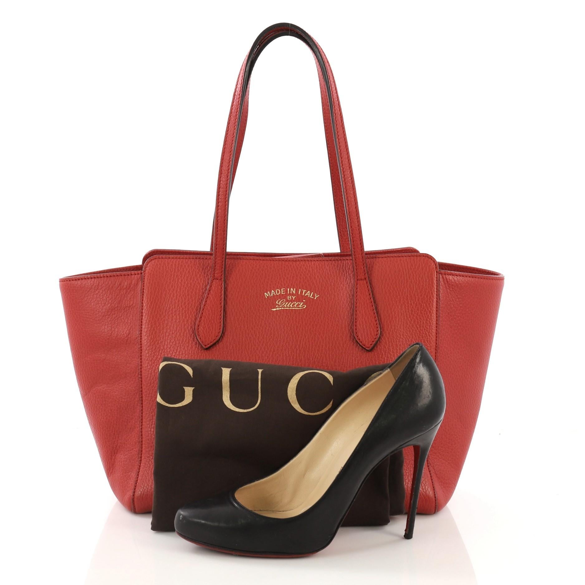 This Gucci Swing Tote Leather Small, crafted in red leather, features dual slim handles, Gucci stamped logo at the front, expanded wing silhouette, and gold-tone hardware. Its hidden magnetic snap closure opens to a beige fabric interior with slip