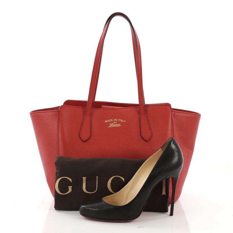 This Gucci Swing Tote Leather Small, crafted in red leather, features dual slim handles, Gucci stamped logo at the front, expanded wing silhouette, and gold-tone hardware. Its hidden magnetic snap closure opens to a beige fabric interior with zip