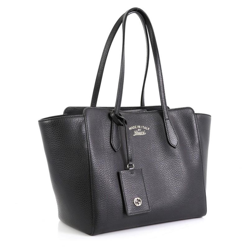 This Gucci Swing Tote Leather Small, crafted in black leather, features dual slim handles, Gucci stamped logo at the front and gold-tone hardware. Its hidden magnetic snap closure opens to a neutral fabric interior with zip and slip pockets.