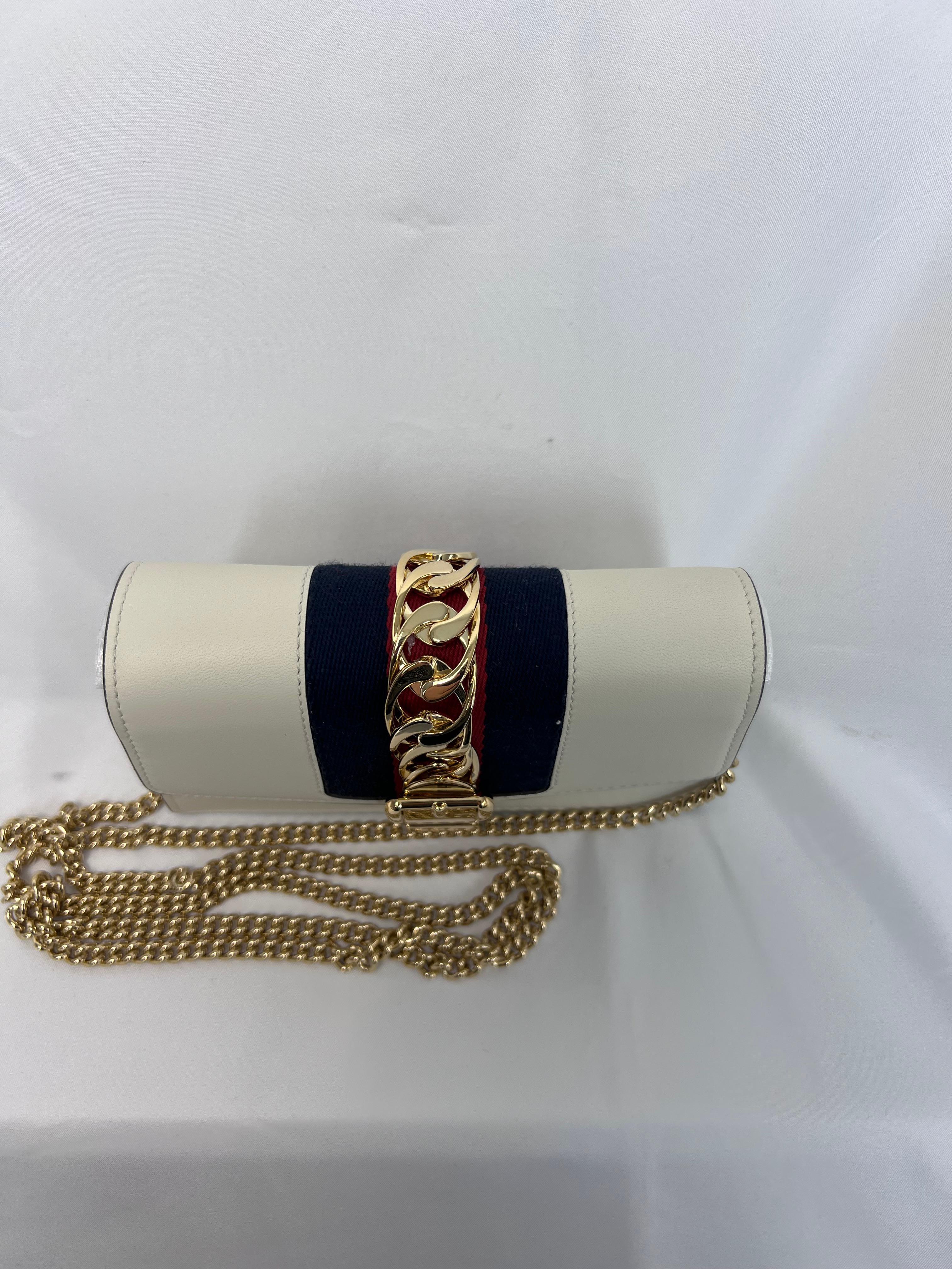 The Gucci Sylvie Chain Leather Crossbody Bag is a compact and elegant accessory that perfectly combines timeless sophistication with modern flair. Crafted from smooth, luxurious leather, this bag features the signature Sylvie web stripe detail