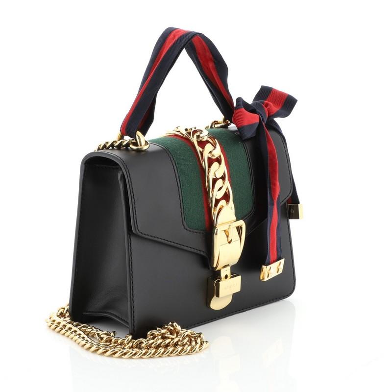 This Gucci Sylvie Chain Shoulder Bag Leather Mini, crafted from black leather, features long chain shoulder strap, nylon Web detail with curb chain, and gold-tone hardware. Its buckle closure opens to a neutral microfiber interior with slip pocket.