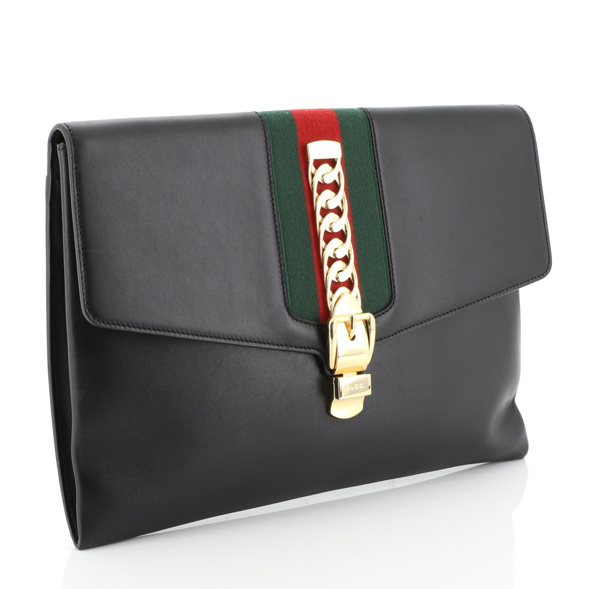 This Gucci Sylvie Clutch Leather Maxi, crafted from black leather, features nylon web detail, curb chain with faux buckle, and gold-tone hardware. Its push-lock closure opens to a neutral microfiber interior with slip pocket. 

Estimated Retail