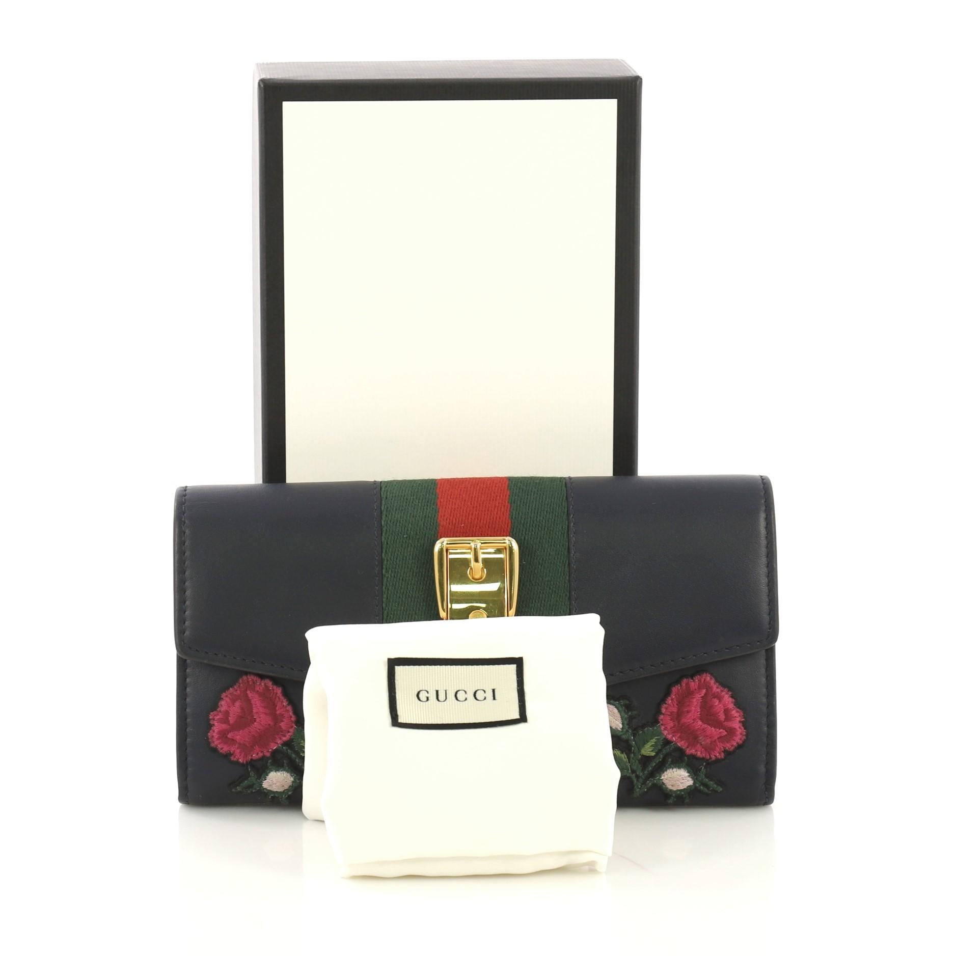 This Gucci Sylvie Continental Wallet Embroidered Leather, crafted from navy embroidered leather, features the signature Gucci web detail with buckle accents and gold-tone hardware. It opens to a navy leather and fabric interior with multiple card