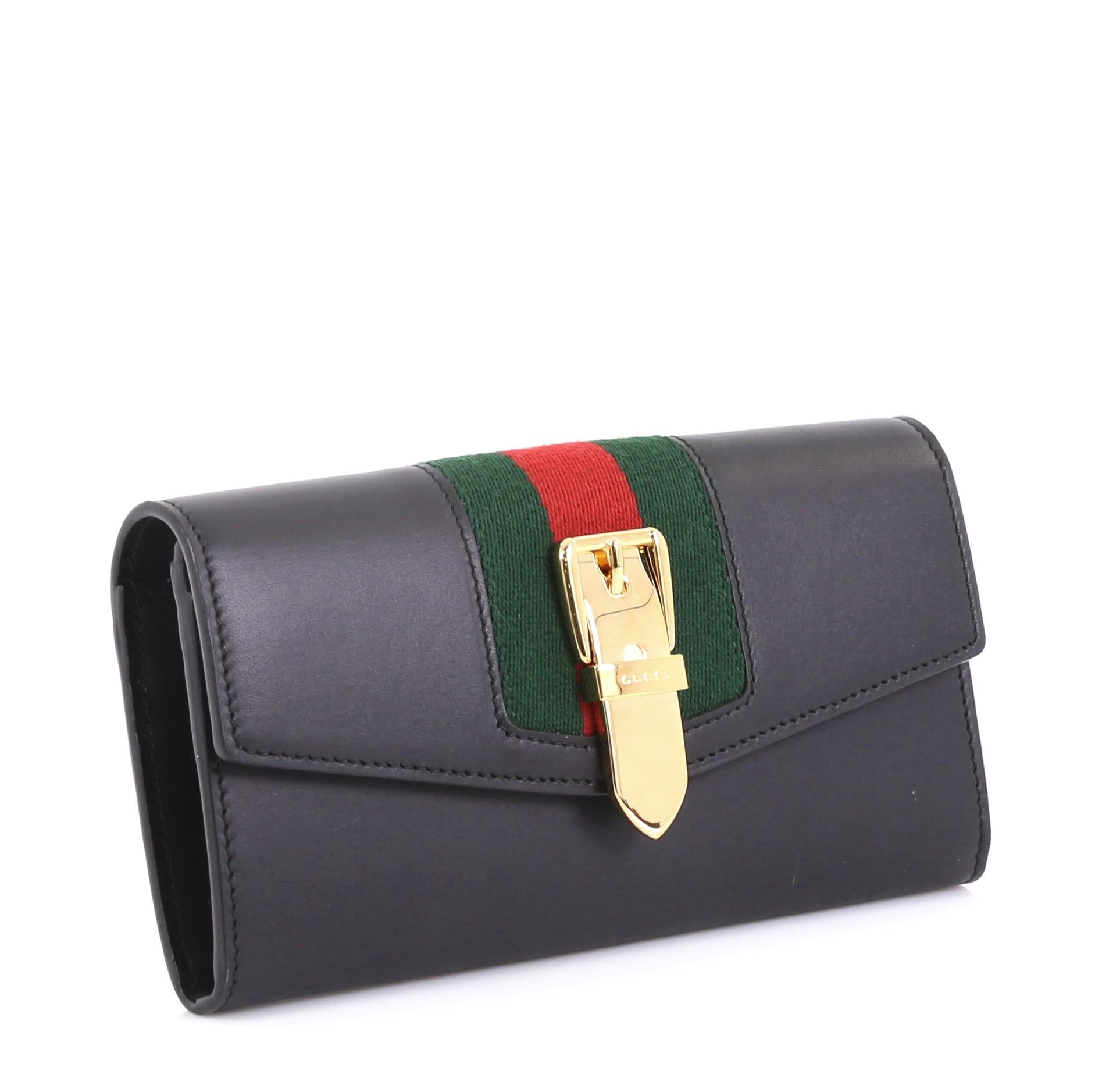 This Gucci Sylvie Continental Wallet Leather, crafted from black leather, features a nylon web detail with buckle and gold-tone hardware. It opens to a black leather interior with multiple card slots and center zip compartment. 

Estimated Retail