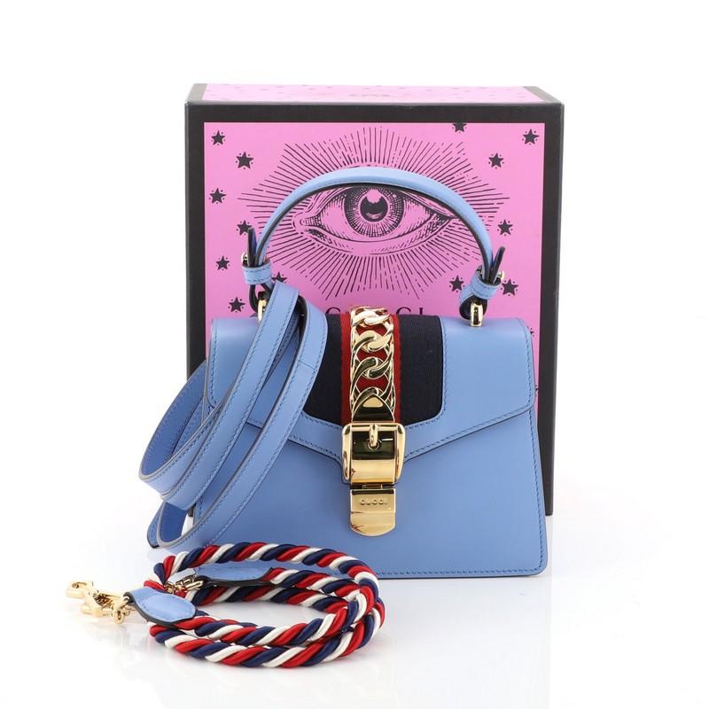 This Gucci Sylvie Top Handle Bag Leather Mini, crafted from blue leather, features a single looped leather handle, nylon web detail with curb chain, and gold-tone hardware. Its buckle closure opens to a neutral microfiber interior with side slip