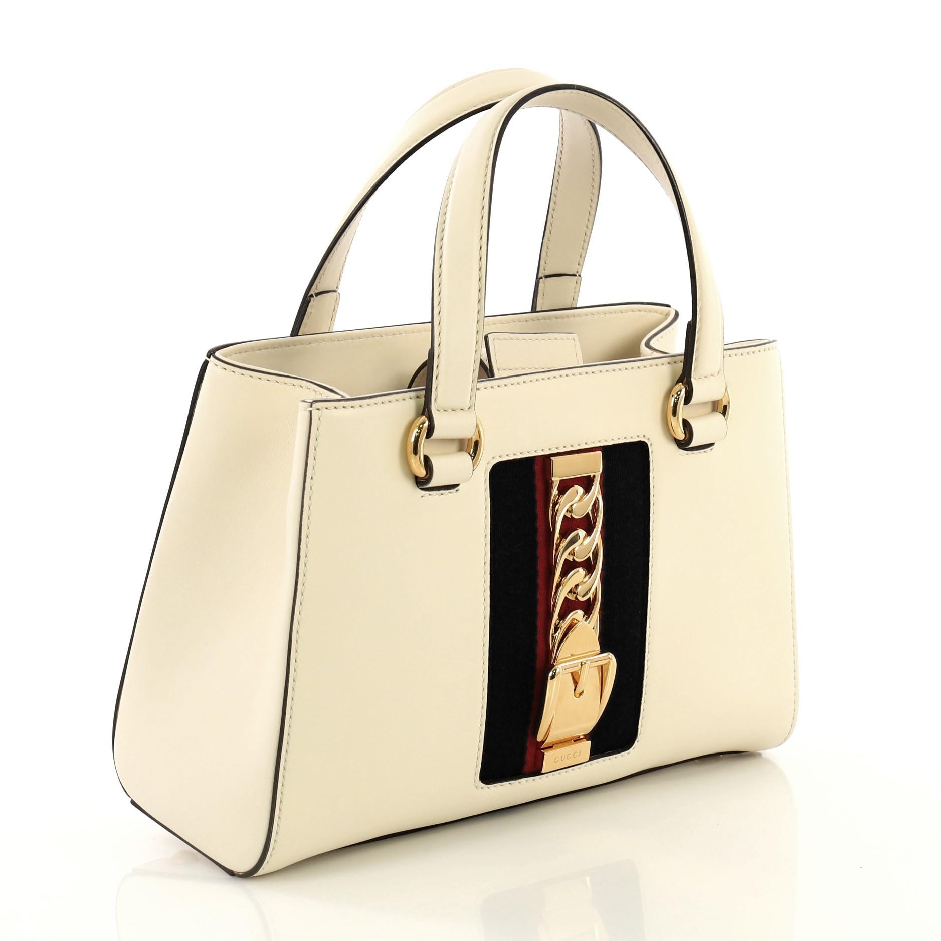 This Gucci Sylvie Top Handle Tote Leather Medium, crafted from white leather, features dual leather handles, nylon web detail with curb chain, and gold-tone hardware. Its magnetic closure opens to a neutral microfiber interior divided into two